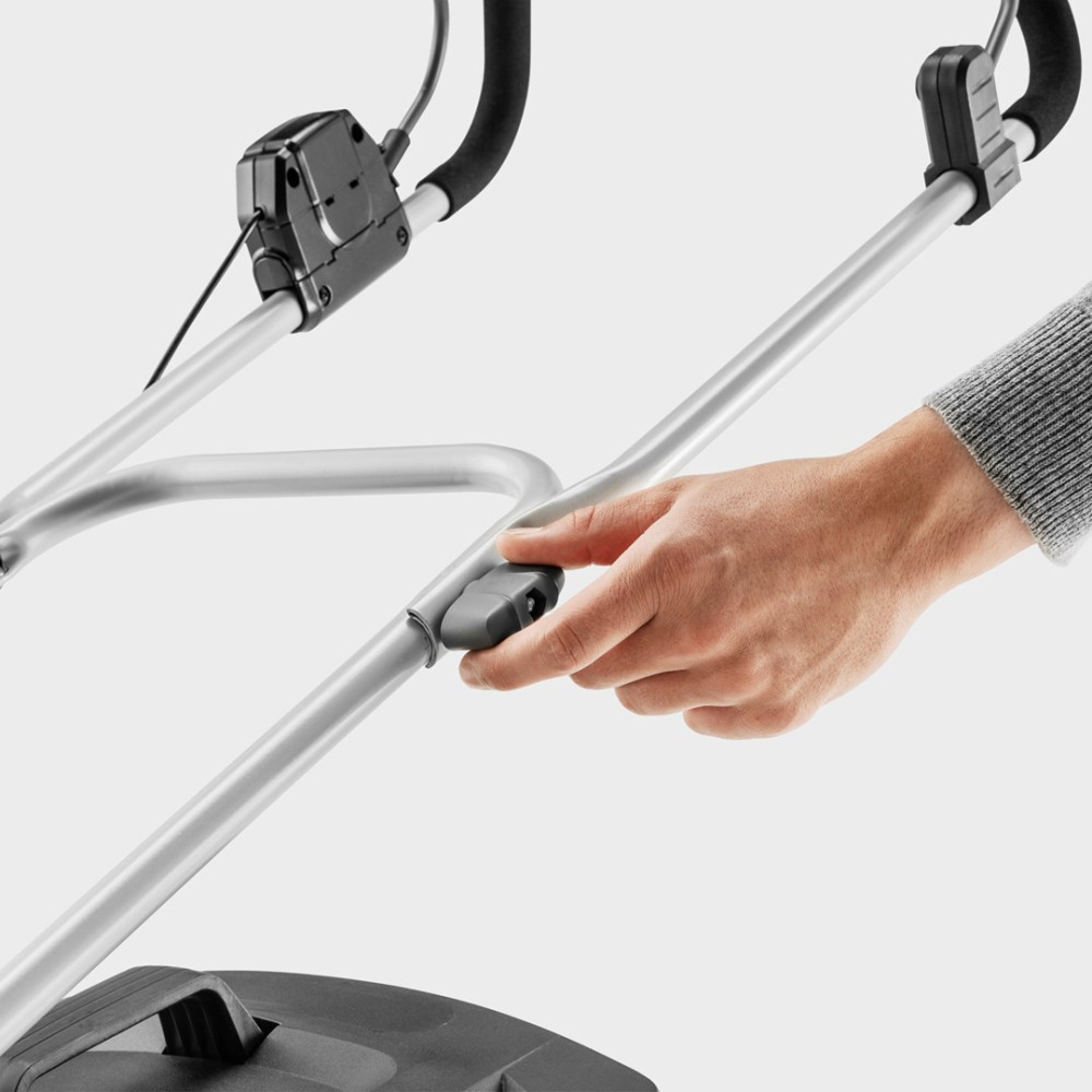 Ręka obraca szary pokrętło na srebrnej rączce kosiarki.