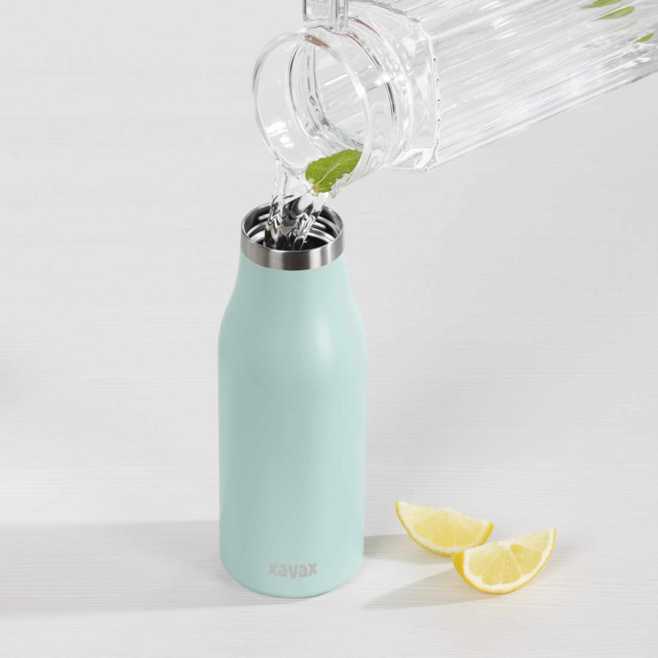 Wasser wird aus einem Glas in eine hellblaue Flasche mit Minze gegossen.