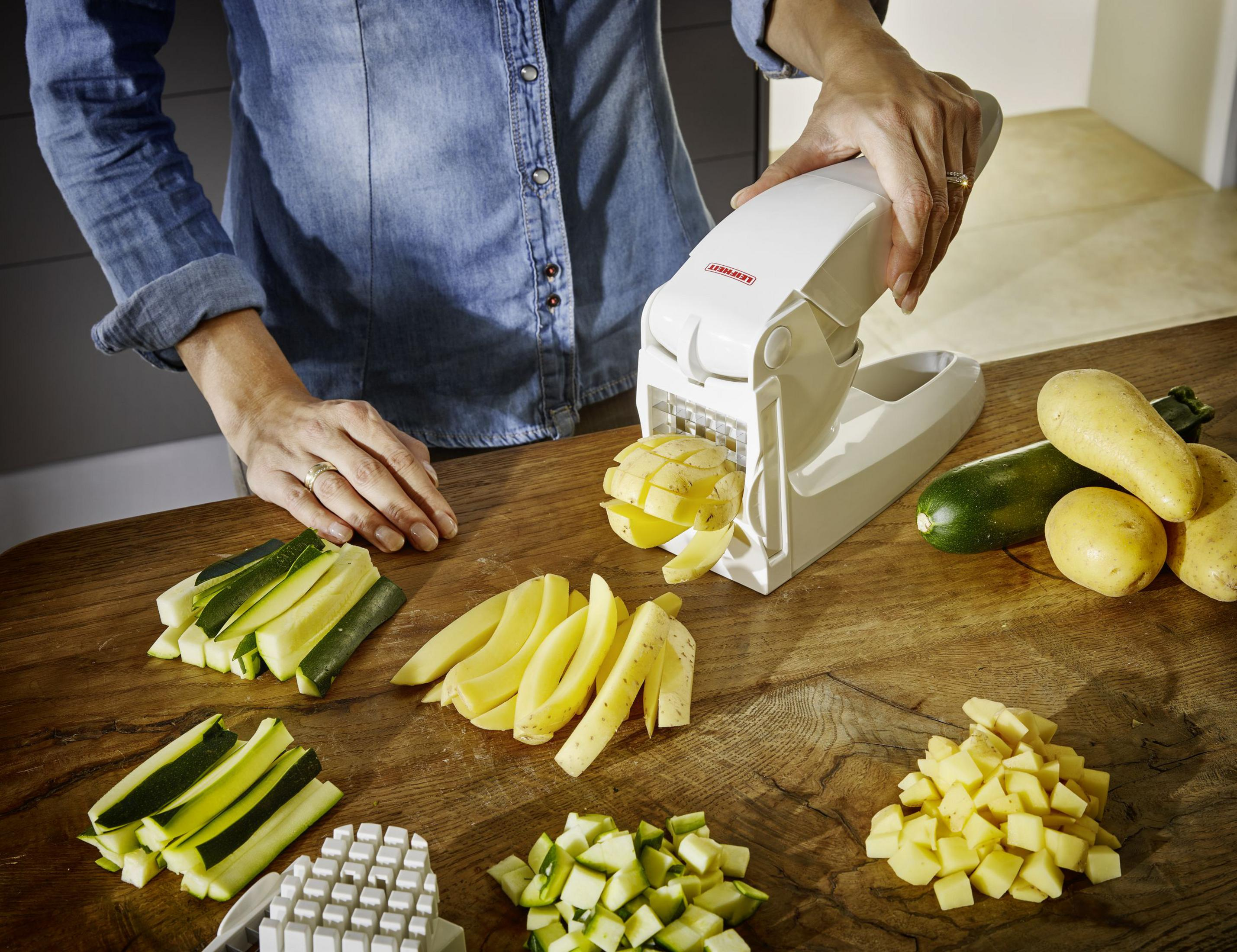 Una persona usa un tagliaverdure bianco per affettare patate e zucchine su un tavolo.