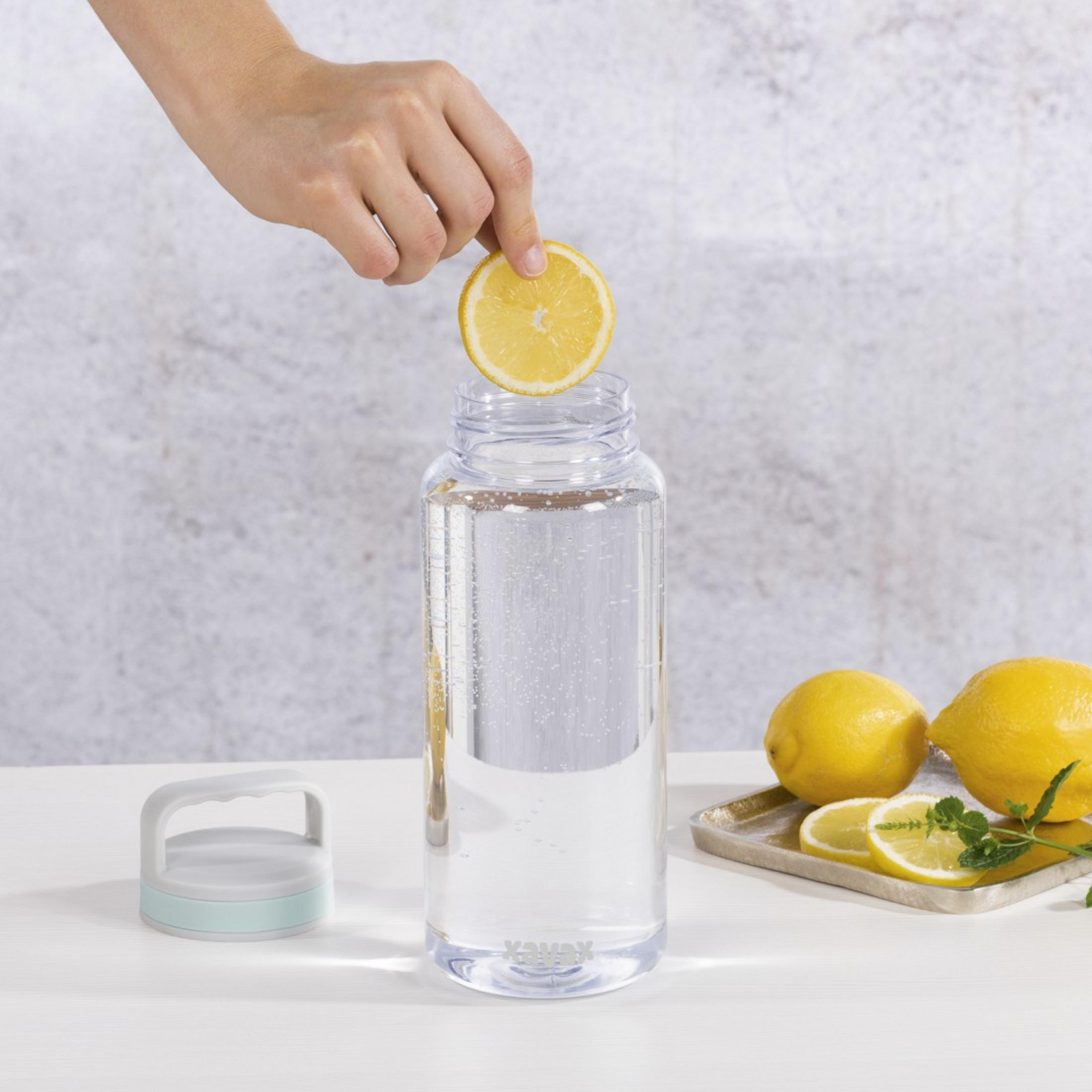Eine Hand gibt eine Zitronenscheibe in eine klare Flasche mit Wasser.