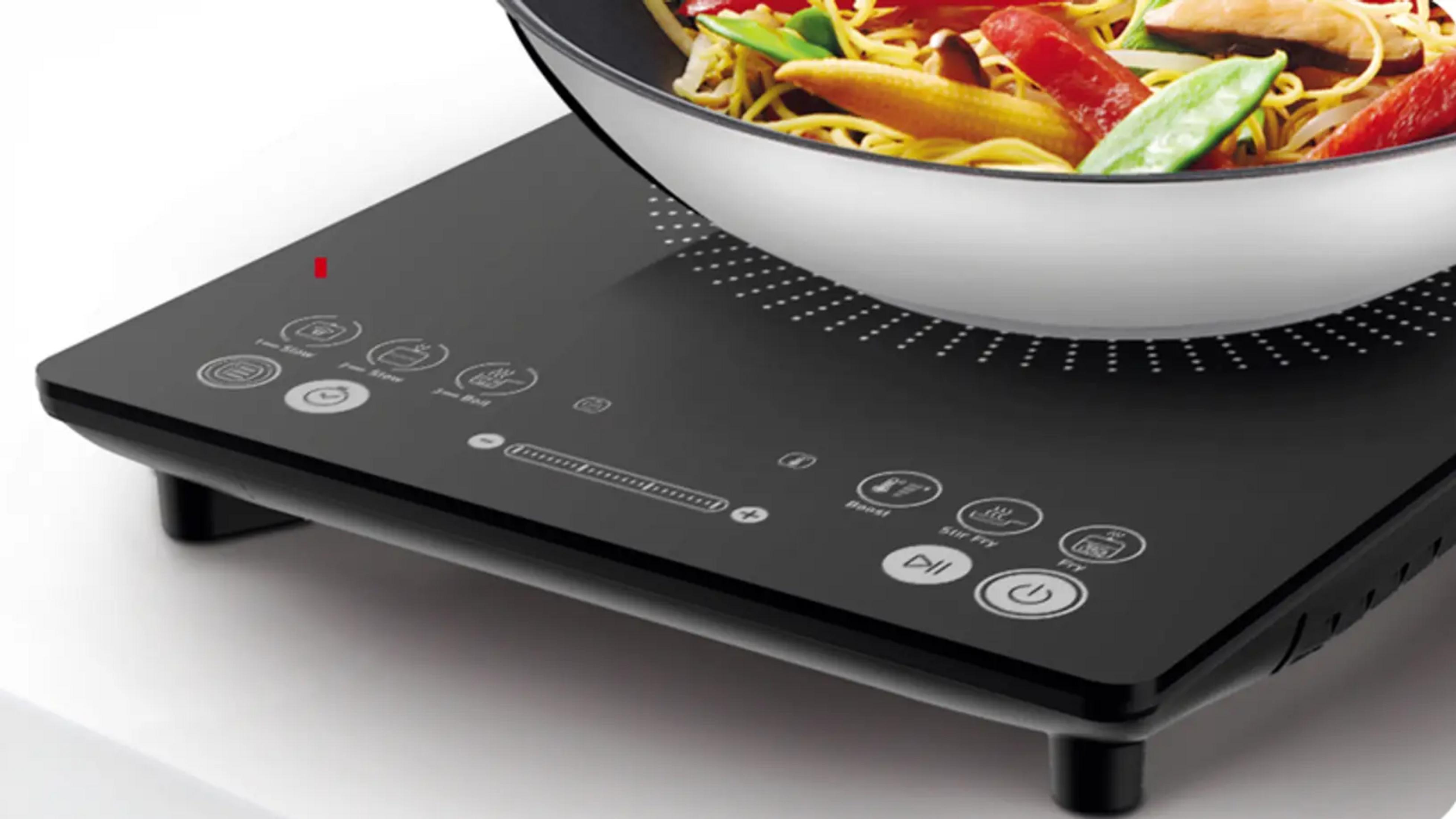 Wok z makaronem i warzywami na czarnej płycie indukcyjnej.