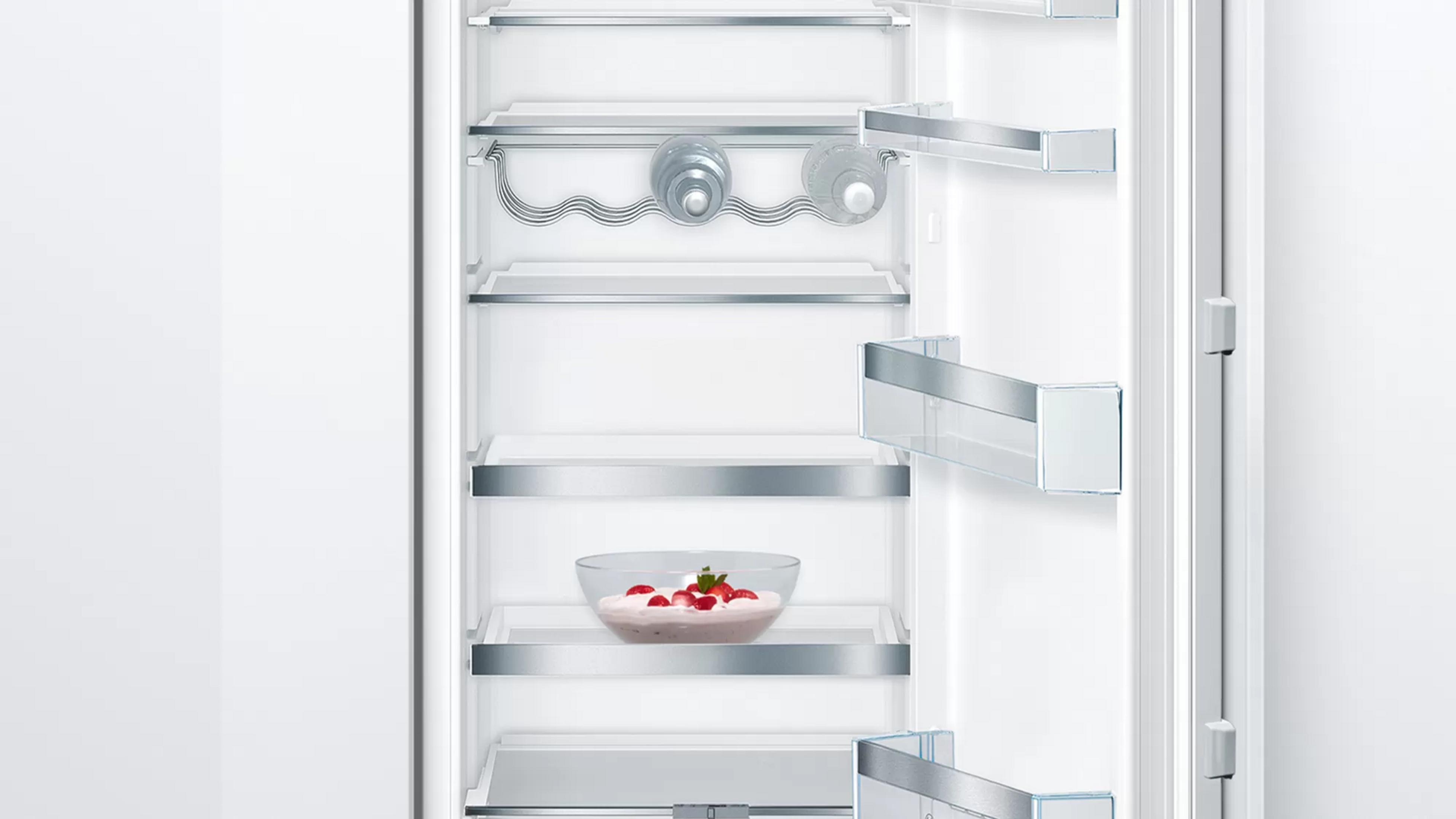 An open refrigerator with a glass bowl of dessert with strawberries on a shelf.