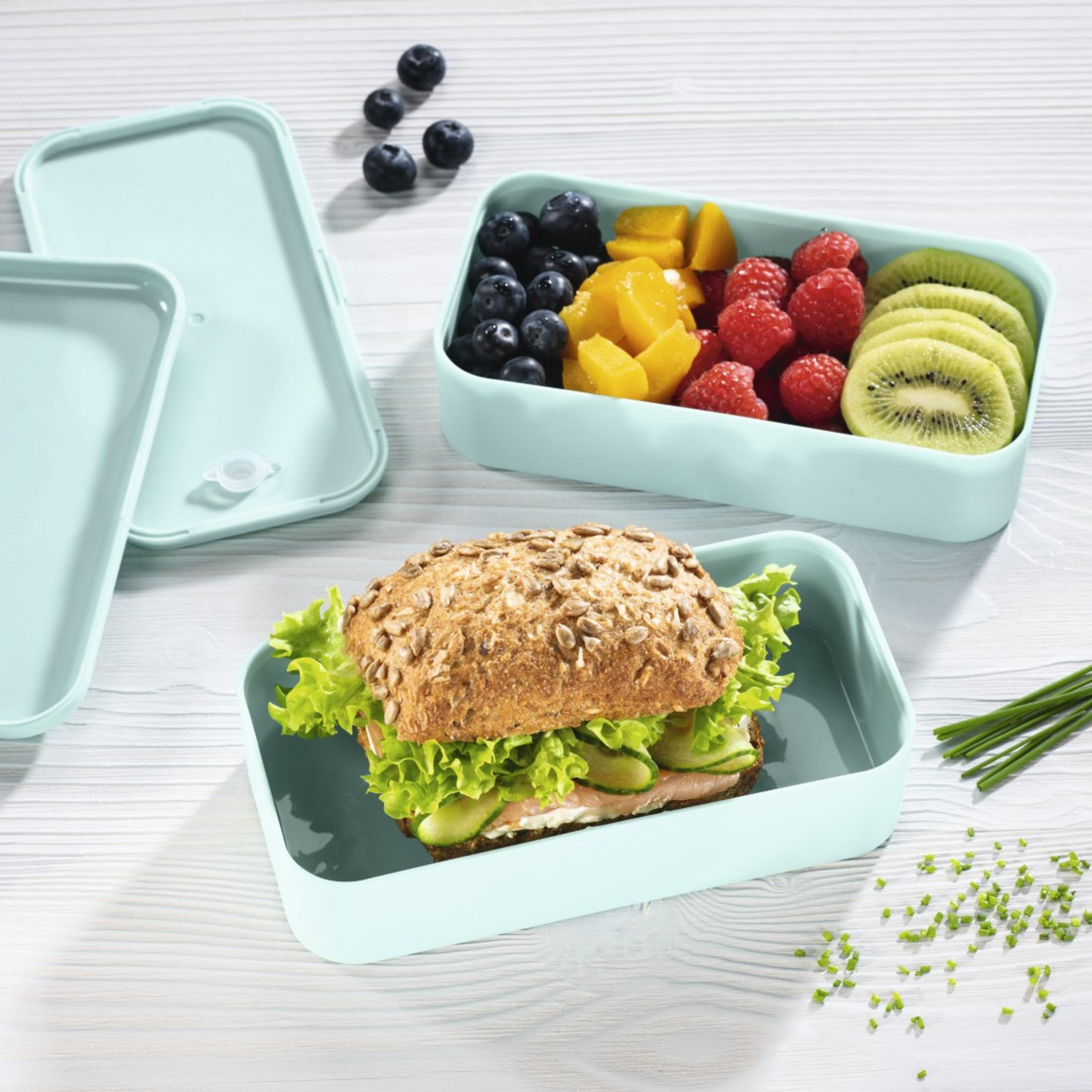 Ein Sandwich und Obst in Behältern auf einem Holztisch.