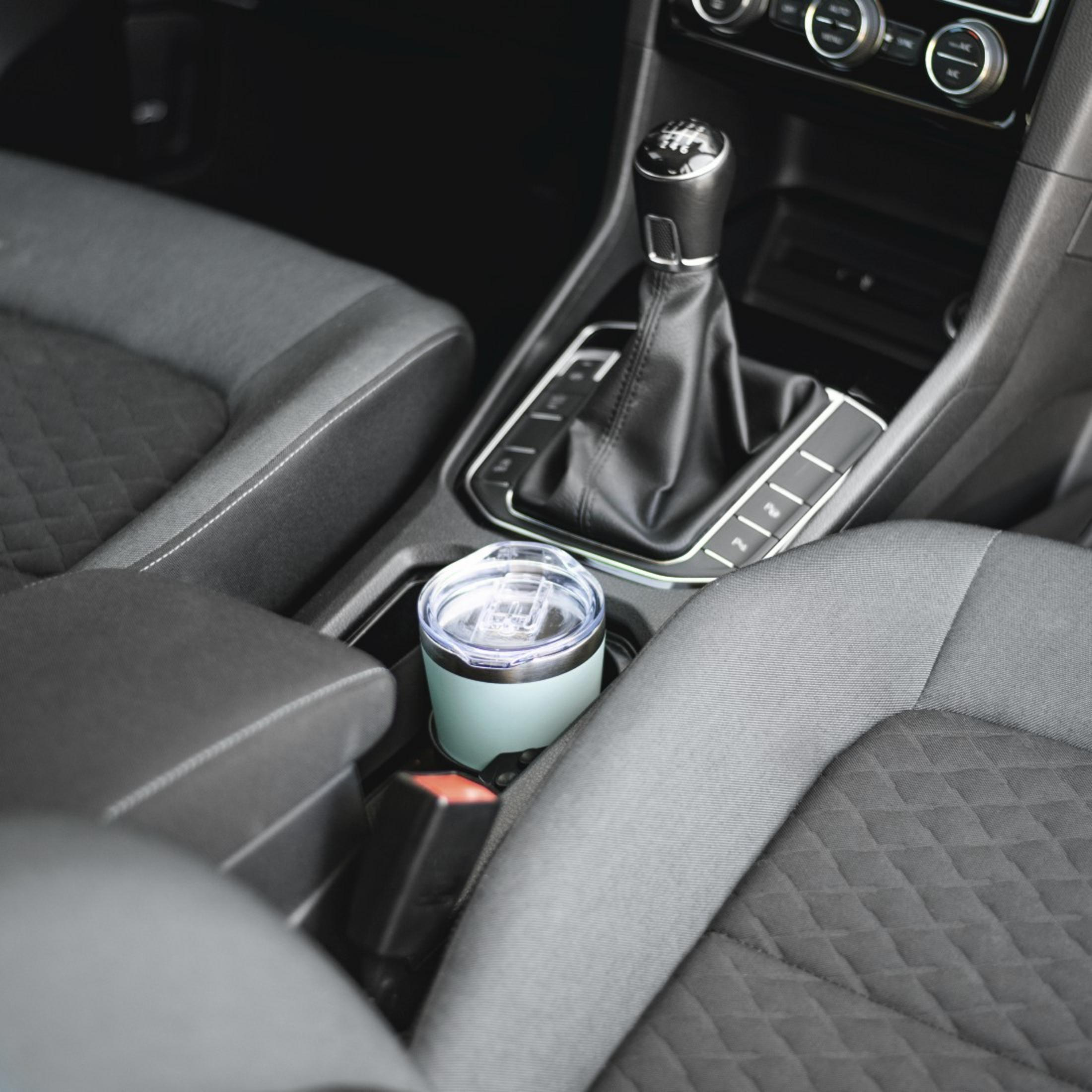 Ein mintgrüner Becher steht im Getränkehalter neben dem Schalthebel eines Autos.
