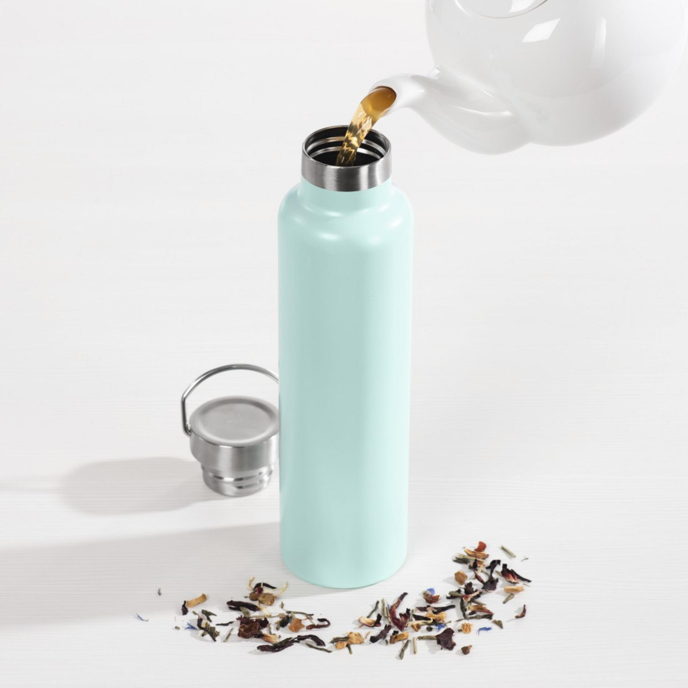 Tee wird aus einer weißen Kanne in eine hellblaue Flasche gegossen.