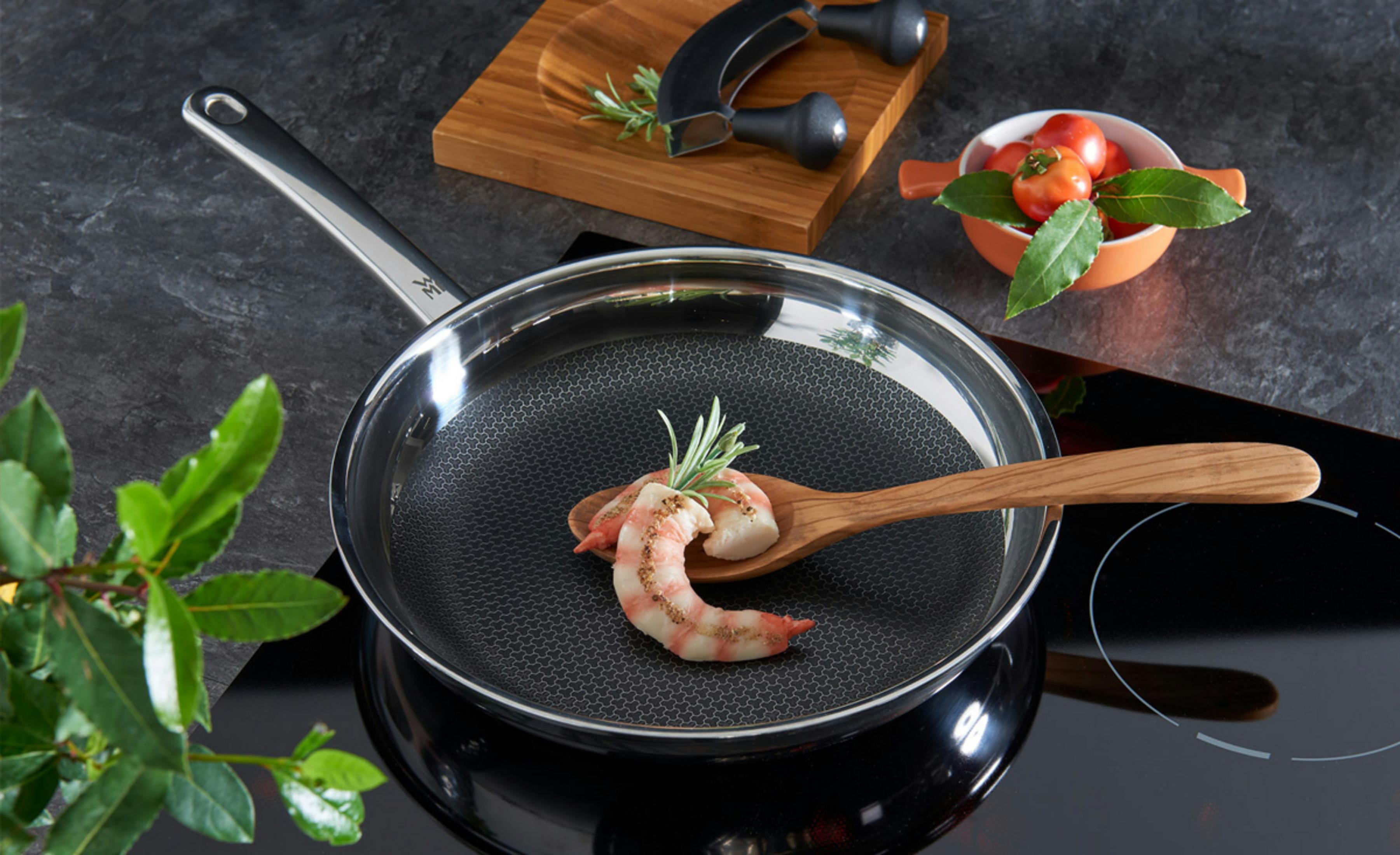 Gotowana krewetka na drewnianej łyżce na patelni, z pomidorami i ziołami.