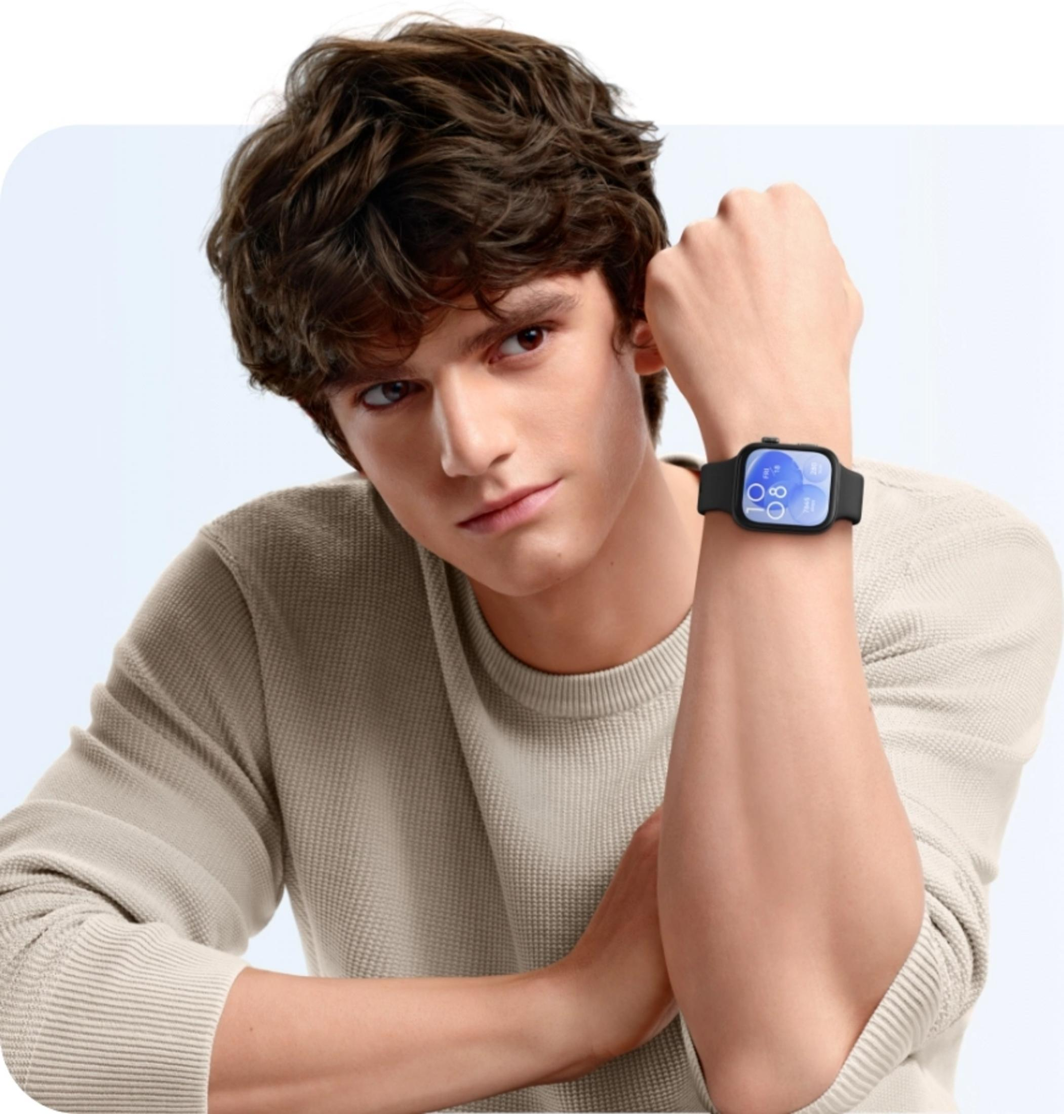 Jonge man met bruin haar draagt een lichtbruine trui en een zwarte smartwatch.