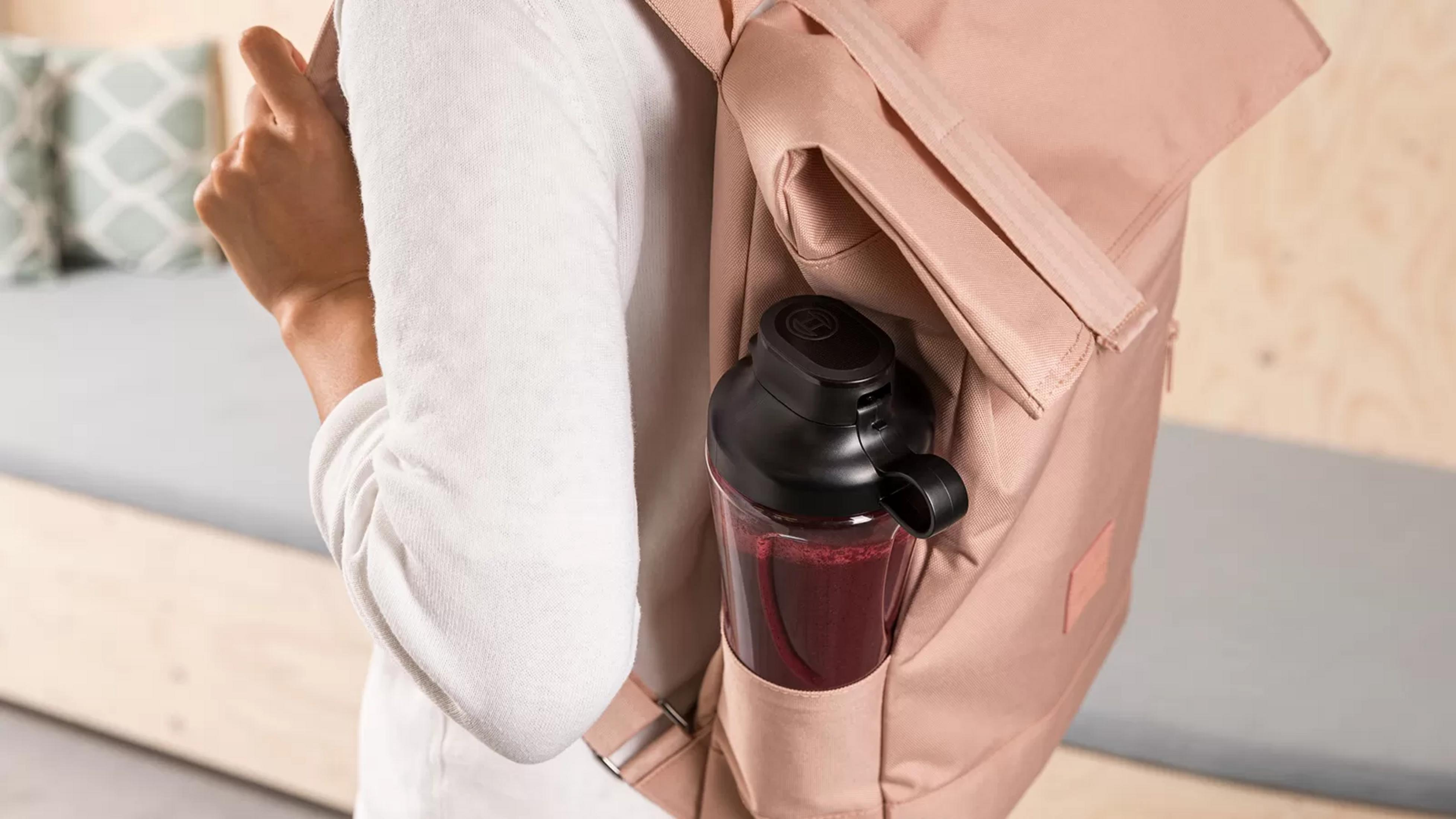 Eine Person trägt einen rosa Rucksack mit einer schwarzen Trinkflasche im Seitenfach.
