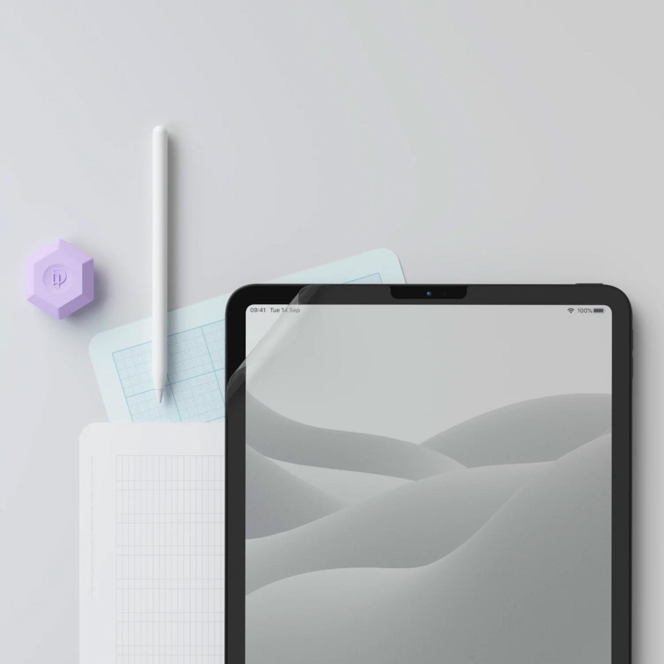Ein Tablet mit Stift, Notizbuch und lila Objekt auf grauem Hintergrund.