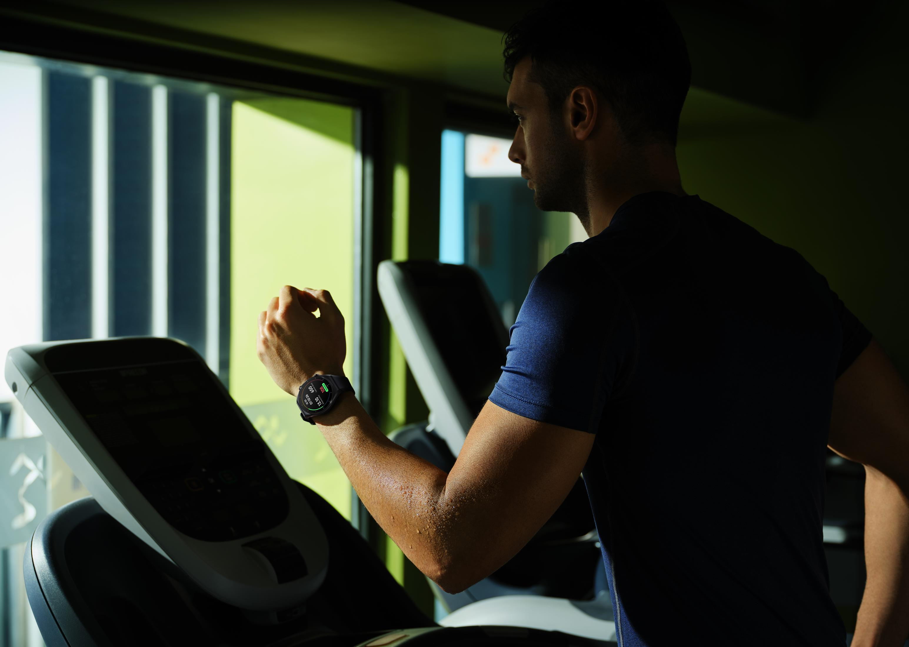 Ein Mann trainiert auf einem Laufband in einem Fitnessstudio, trägt eine Uhr.