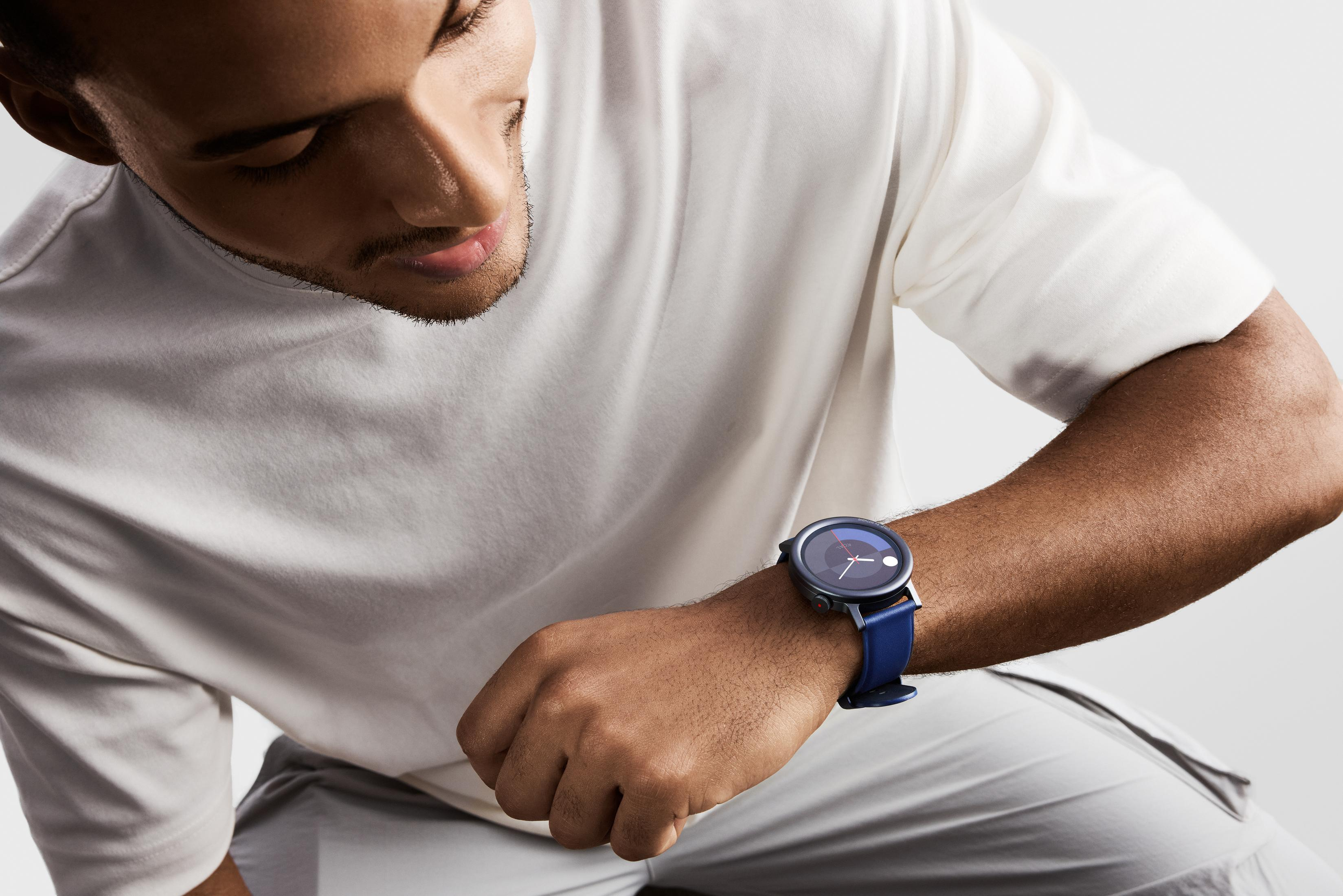Mężczyzna o ciemnej skórze i krótkiej brodzie patrzy na swój niebieski smartwatch.