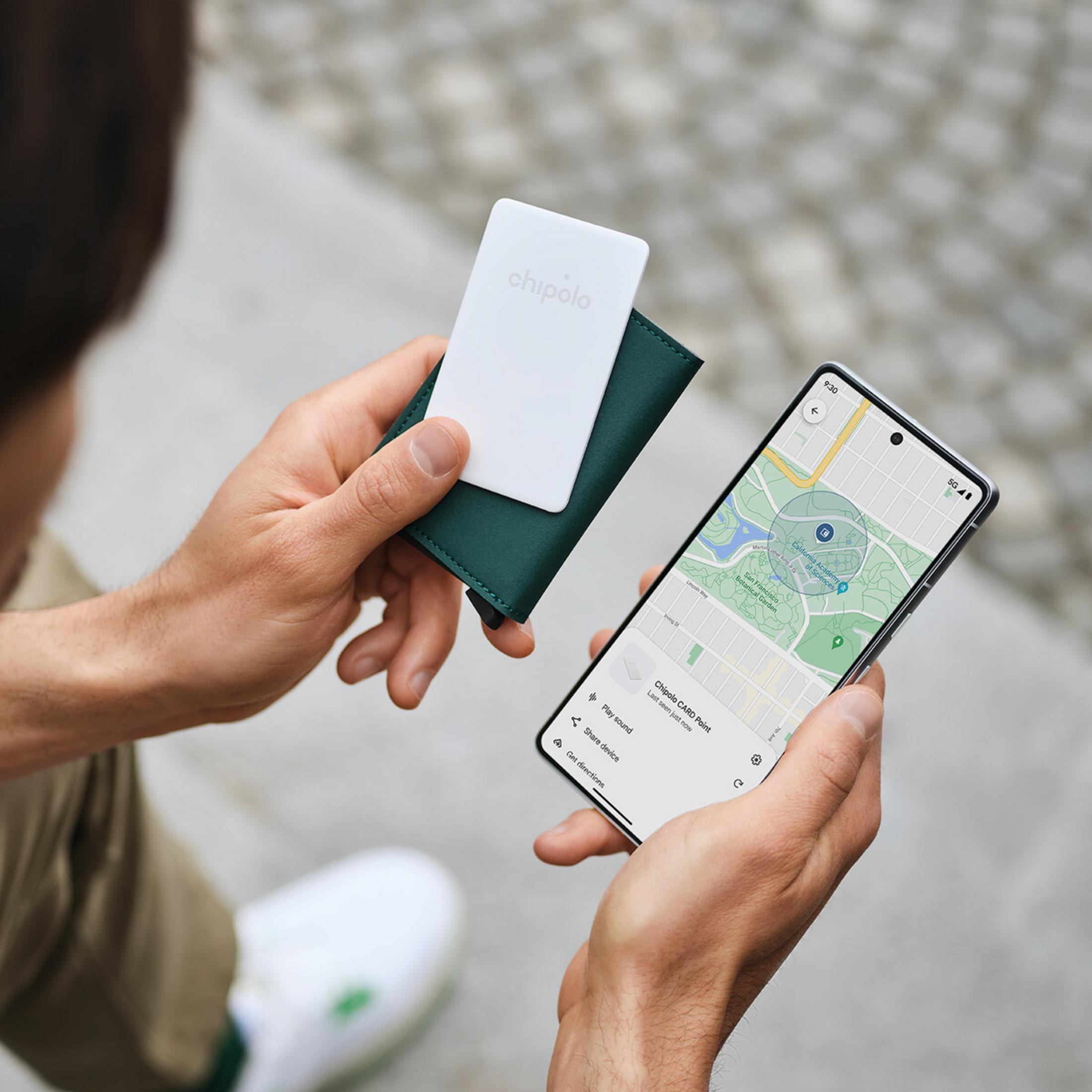 Una persona tiene uno smartphone con una mappa e un tracker Chipolo.