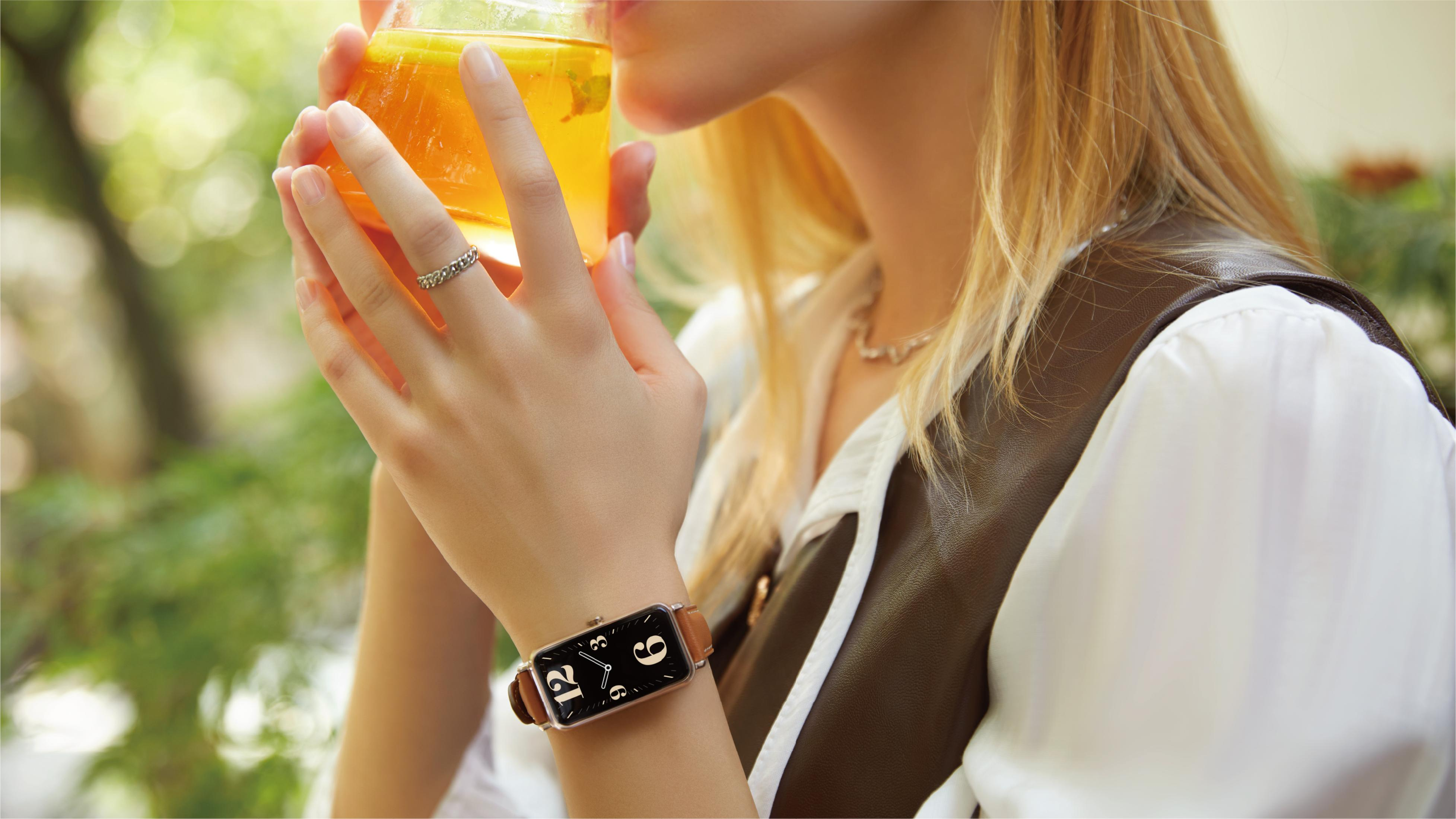 Una donna bionda beve una bevanda gialla. Indossa un orologio.