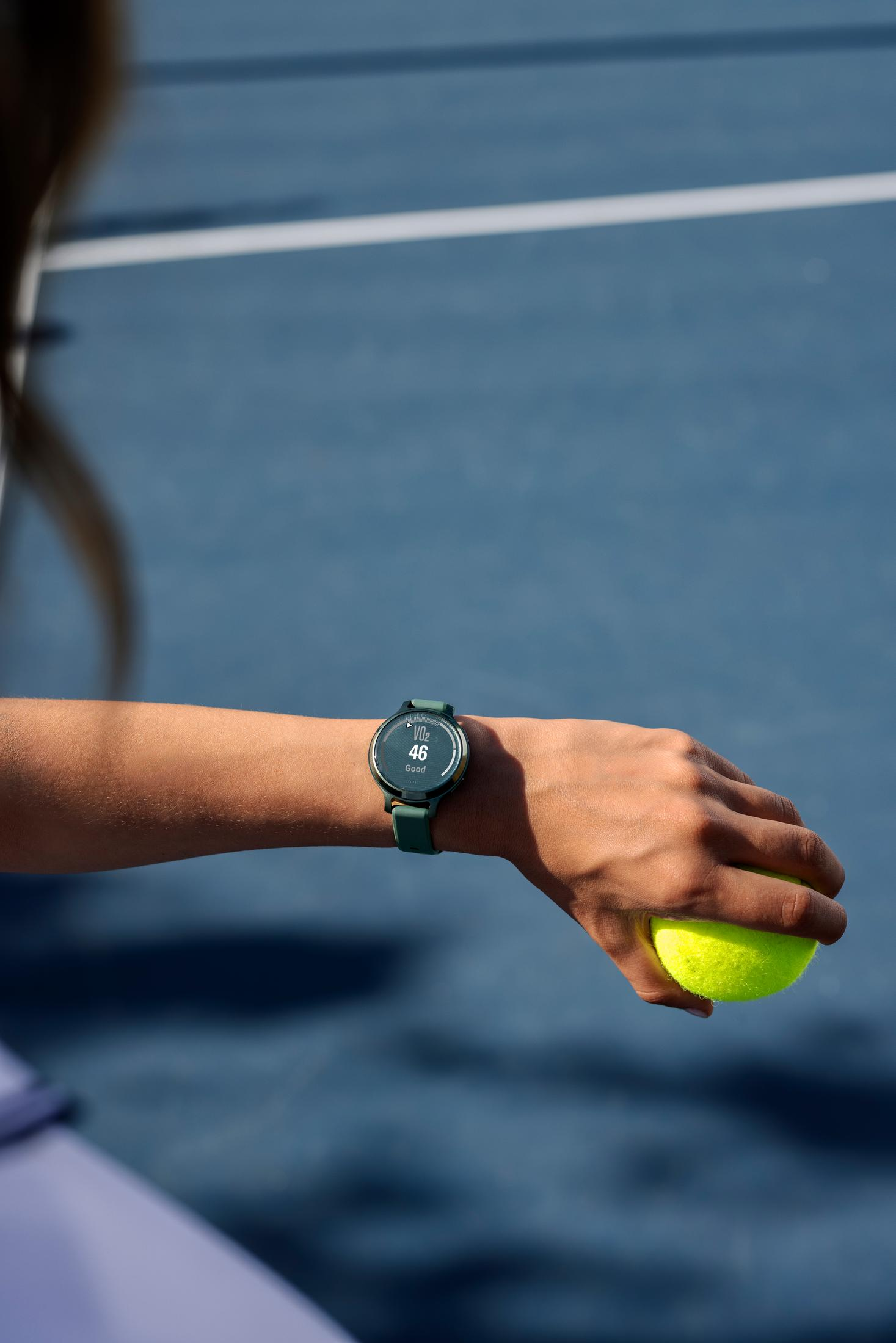 Una mano sostiene una pelota de tenis, un reloj con pantalla de VO2 máx en la muñeca.