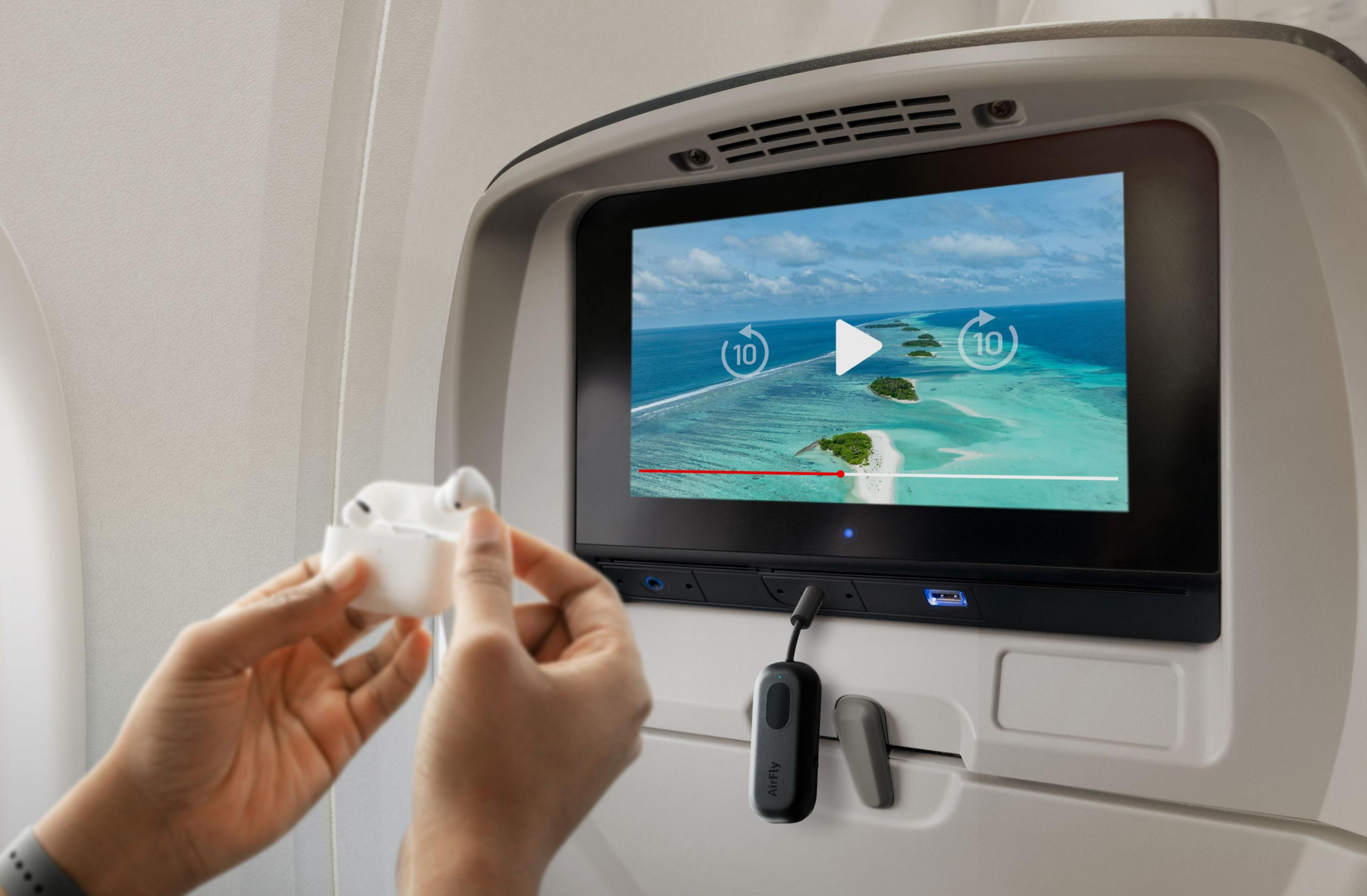 Eine Person nimmt weiße Kopfhörer aus einer Ladehülle vor einem Flugzeugbildschirm.