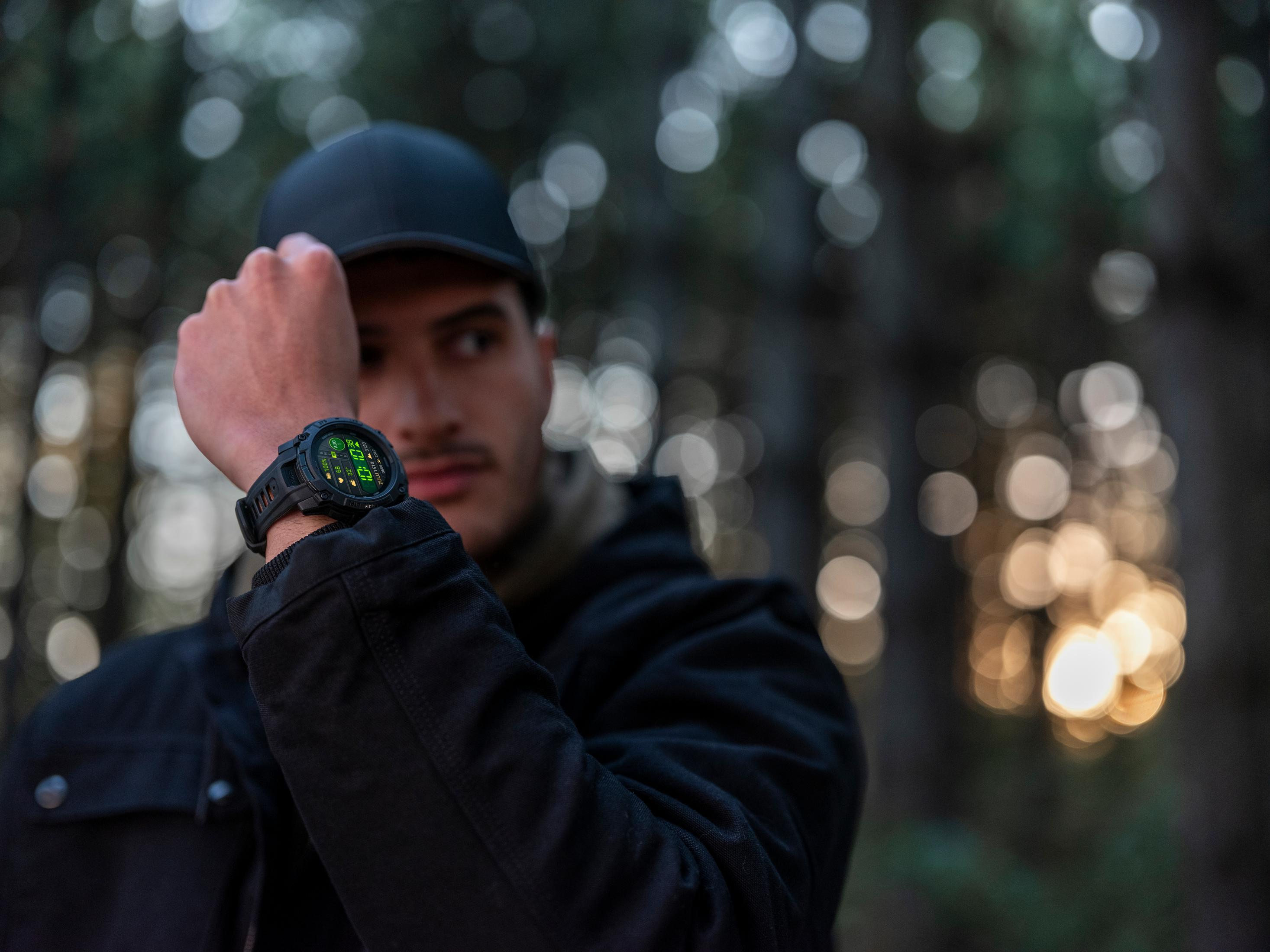 Mężczyzna w czarnej czapce i kurtce pokazuje smartwatch w lesie.