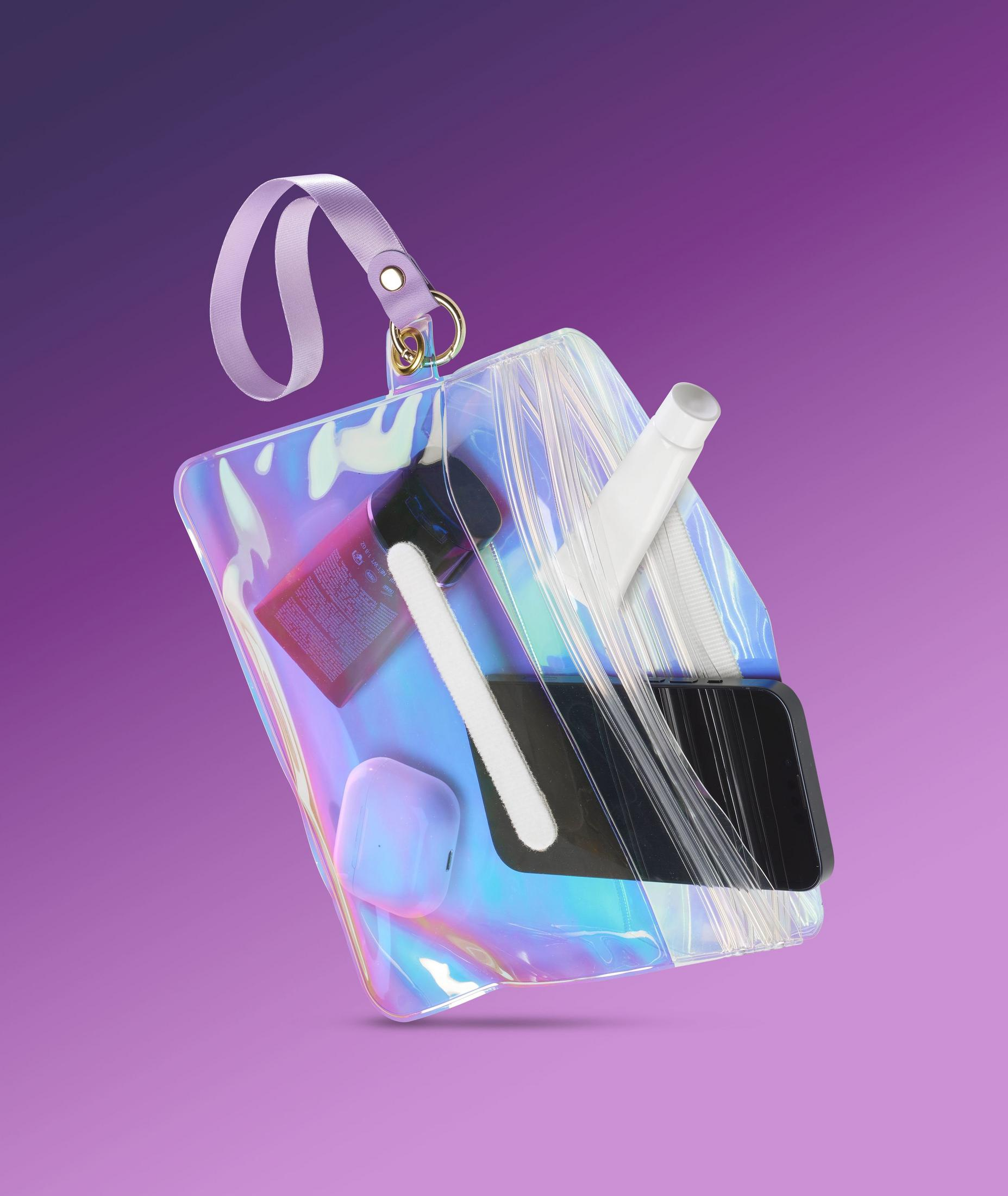 Borsa trasparente iridescente con trucco, telefono e auricolari su sfondo viola.