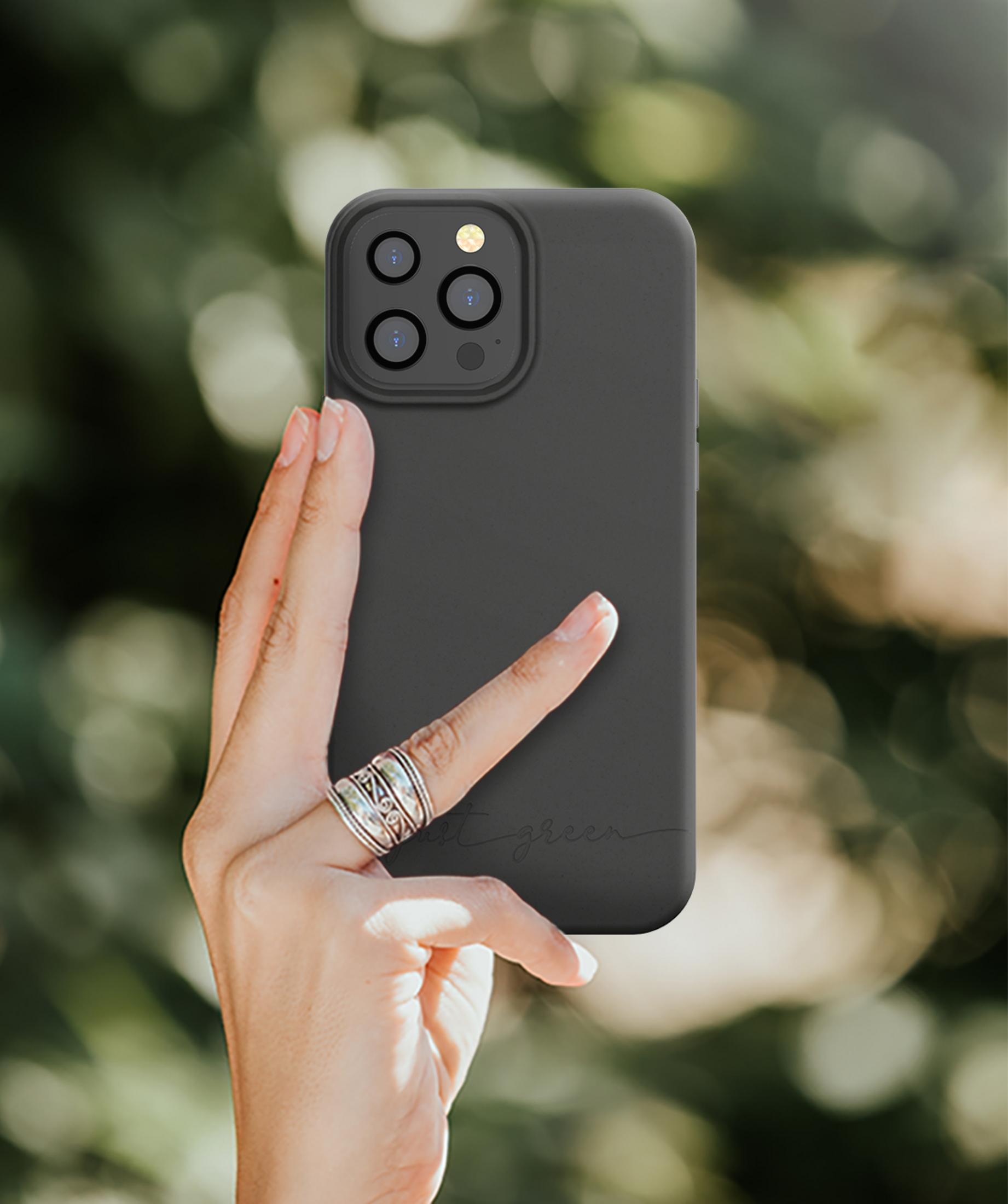 Una mano tiene un telefono nero con obiettivi. Lo sfondo è una vegetazione verde sfocata.