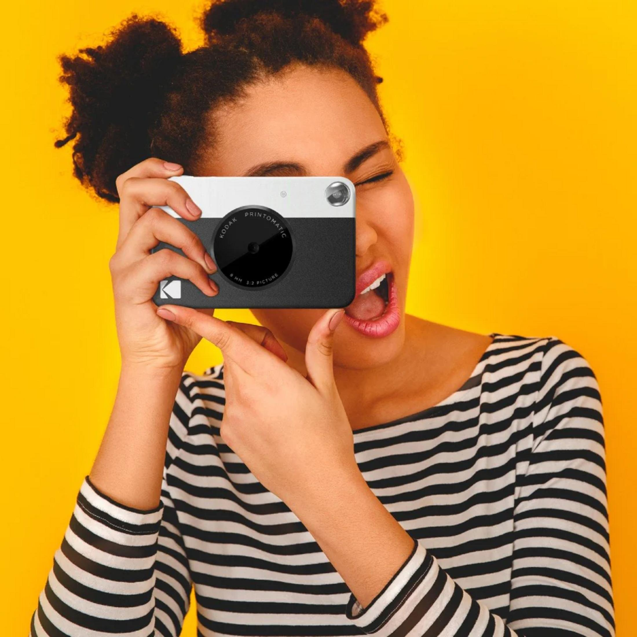 Donna con capelli afro tiene una Kodak su sfondo giallo.
