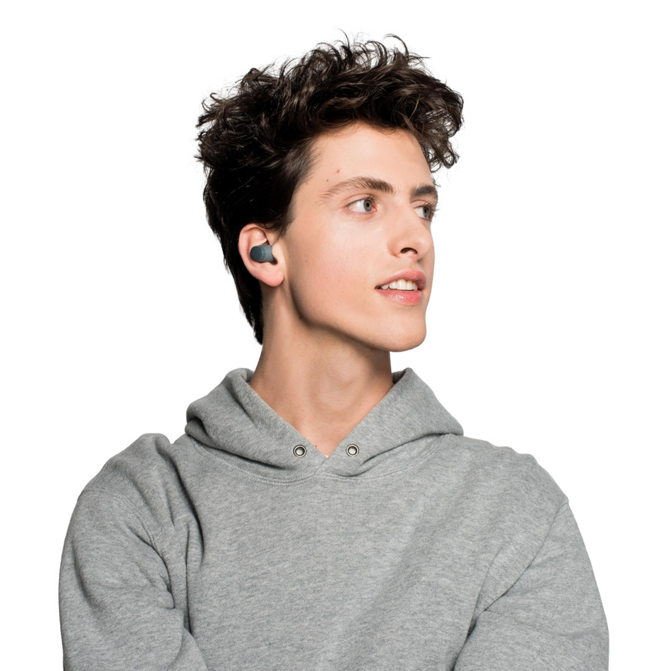 Un joven con cabello oscuro lleva una sudadera gris y auriculares.