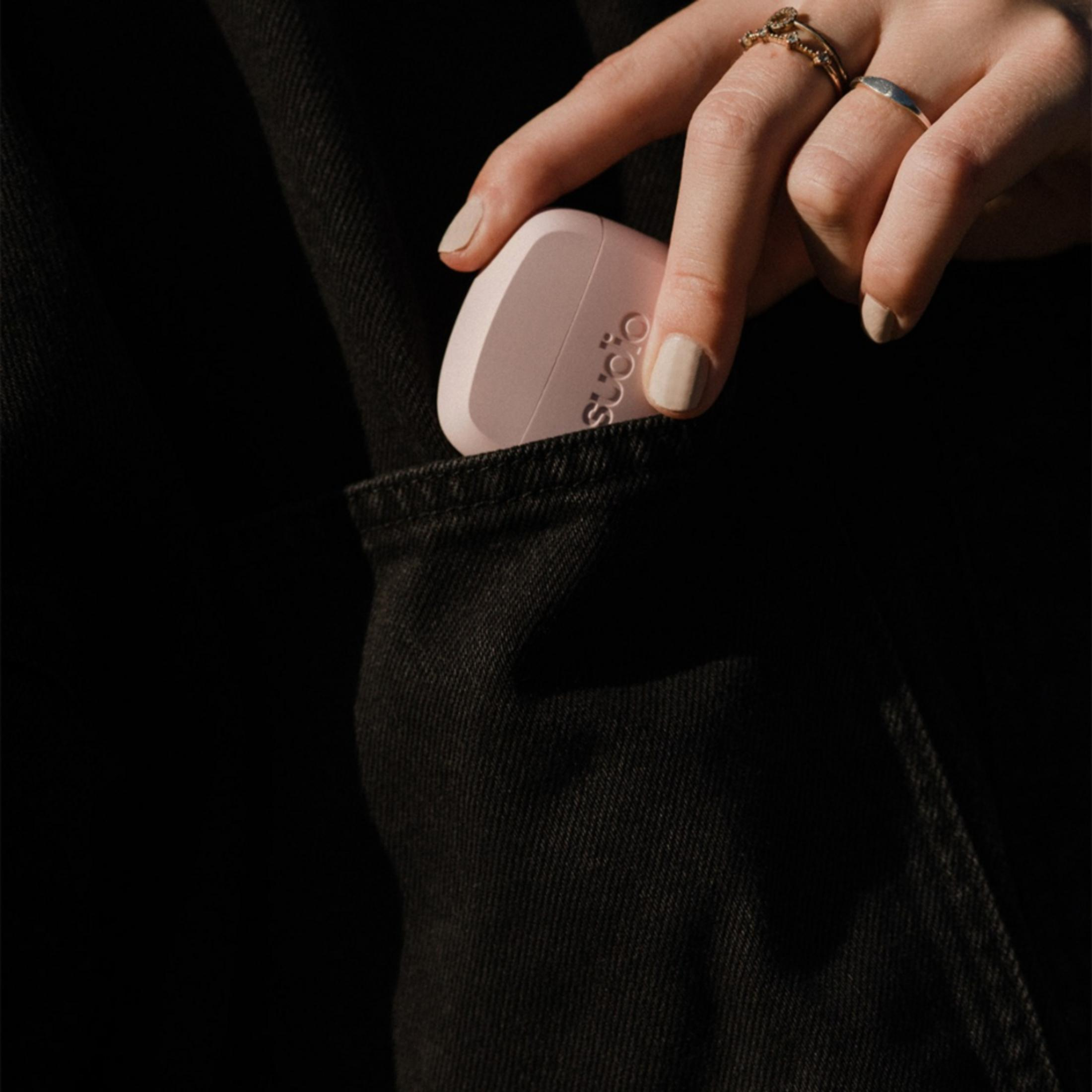 Una mano con anelli infila una custodia rosa in una tasca di jeans nera.