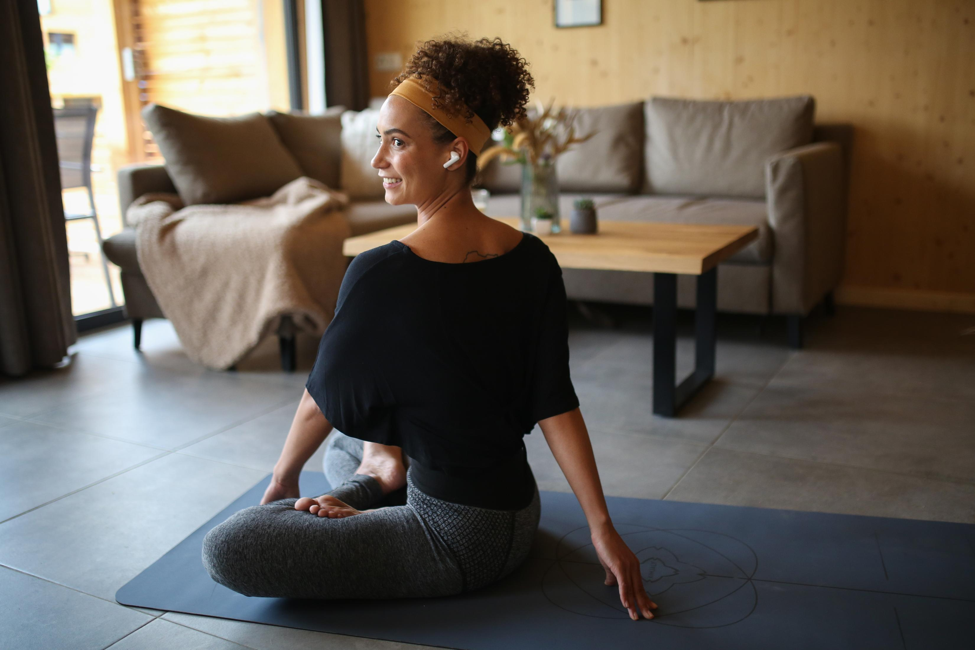 Eine Frau in Schwarz dreht sich auf einer Yogamatte im Wohnzimmer.