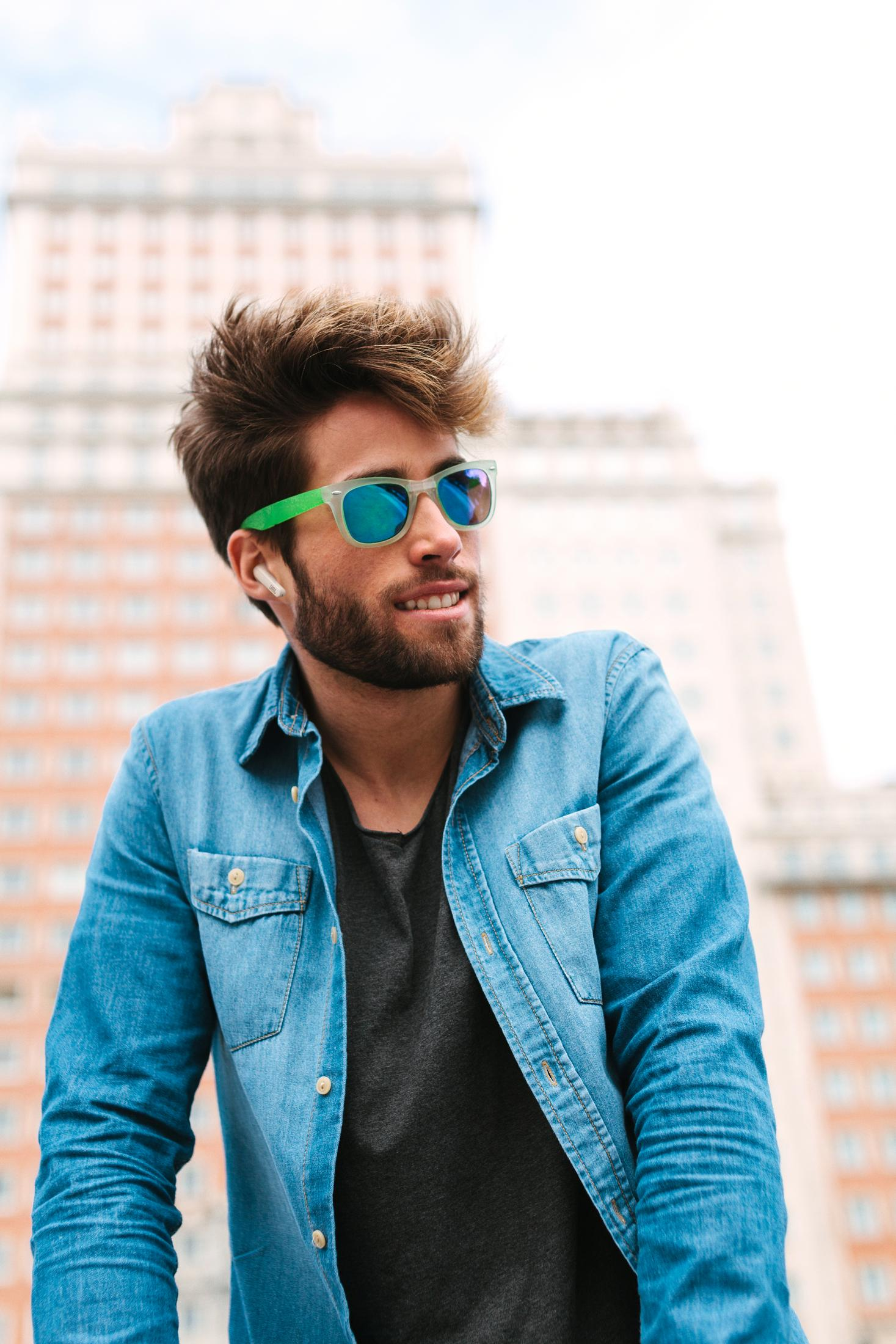 Un uomo con occhiali da sole e auricolari, vestito con una camicia di jeans.