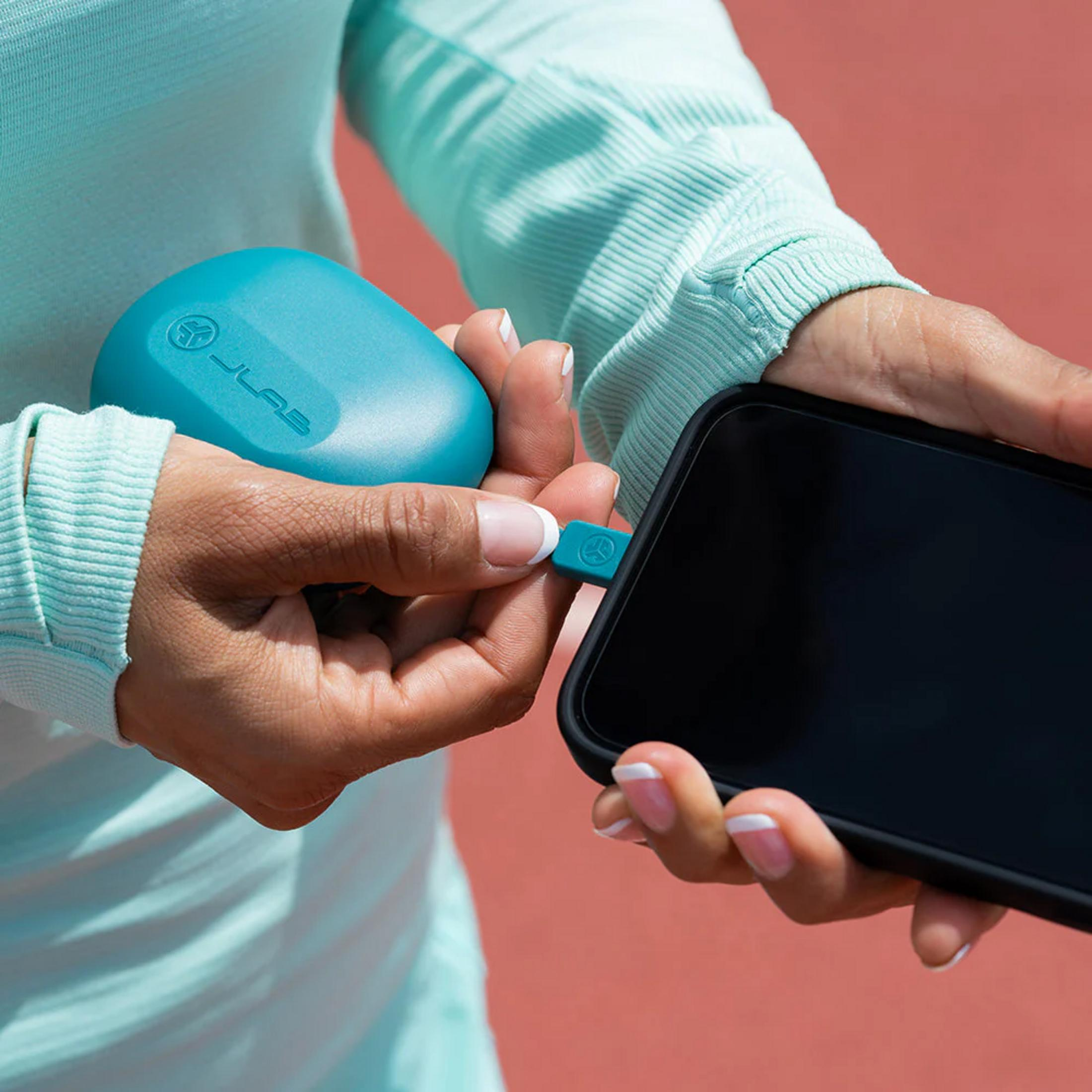 Dłonie podłączają turkusową ładowarkę do smartfona na czerwonym tle.