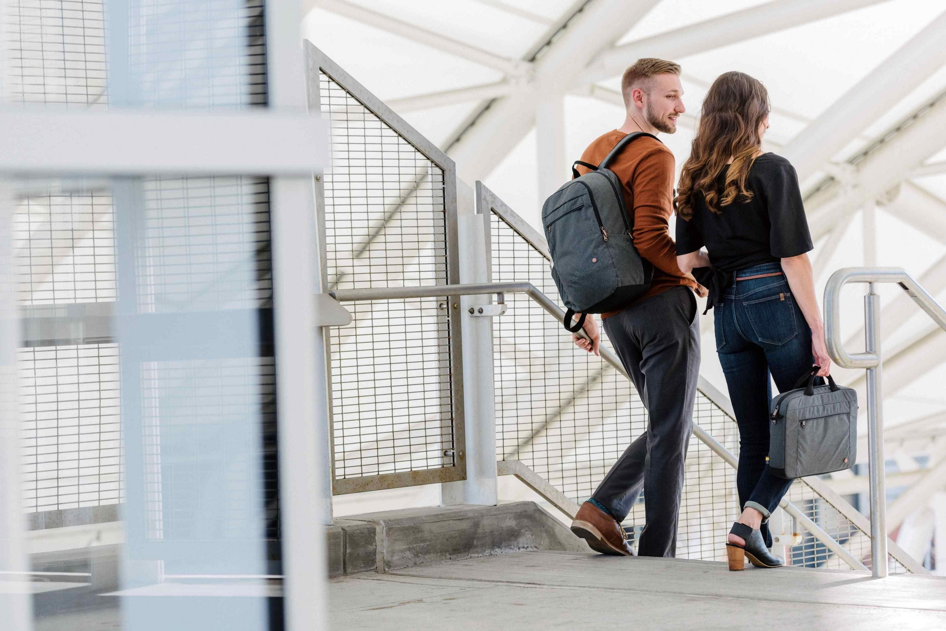 Mann mit Rucksack und Frau mit Tasche gehen Treppen hoch.