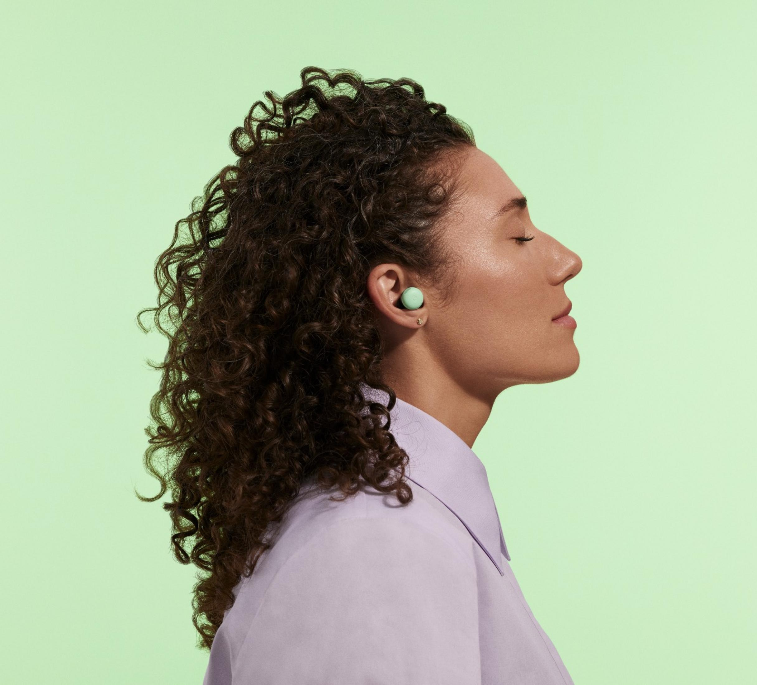 Profil kobiety z kręconymi włosami, noszącej miętowe słuchawki na jasnym tle.