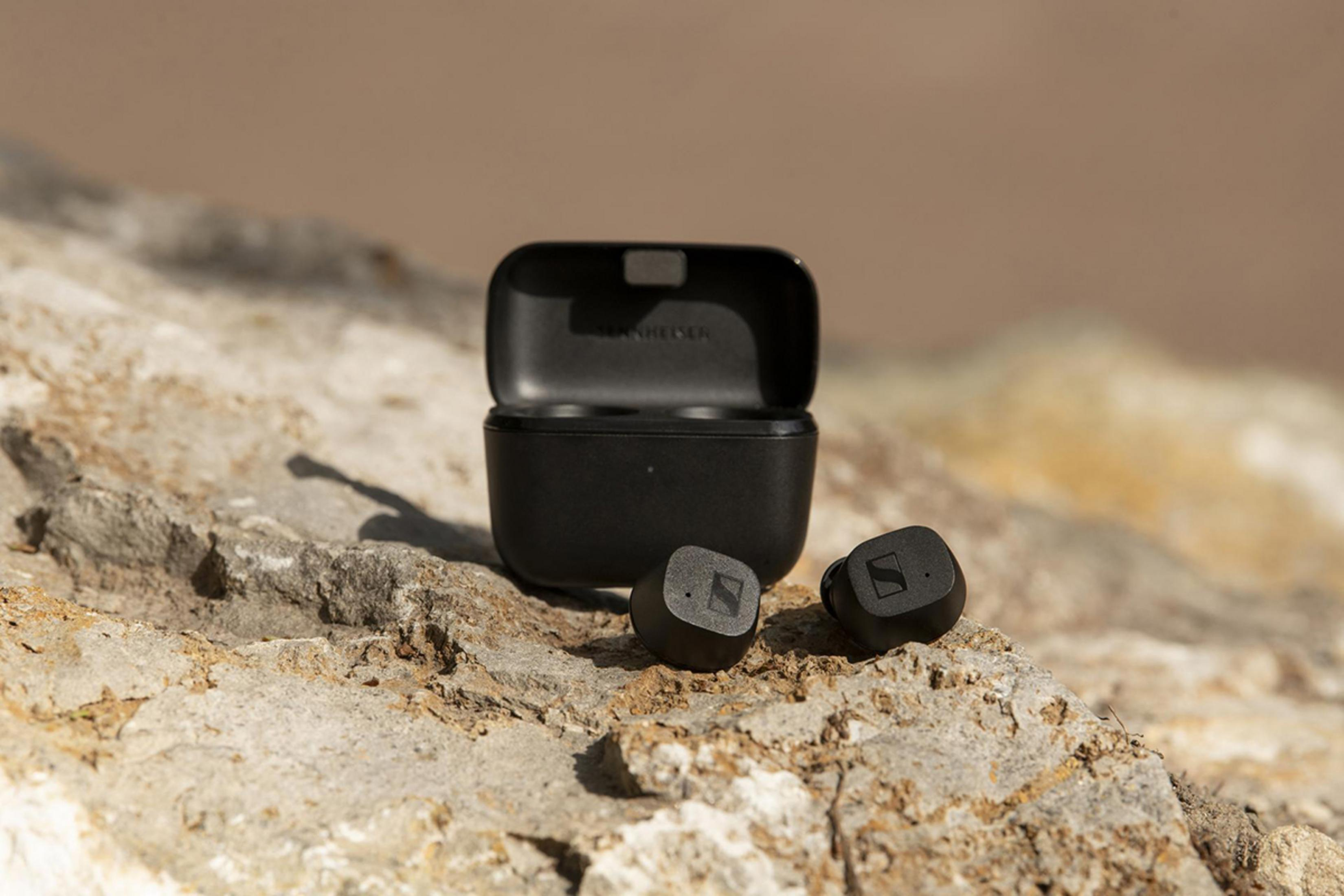 Auriculares y estuche de carga negros sobre rocas.