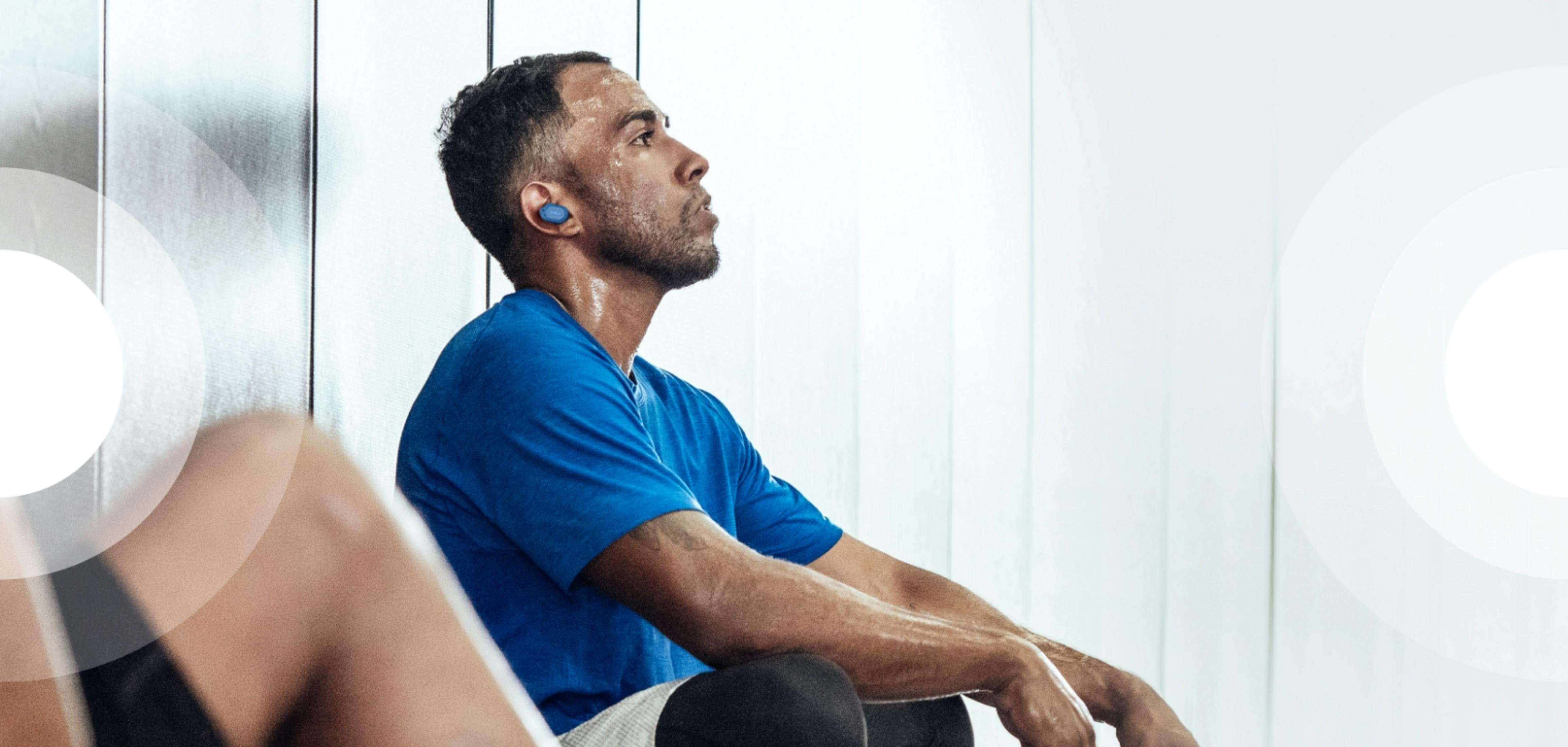 Mężczyzna w niebieskiej koszulce siedzi zmęczony ze słuchawkami.