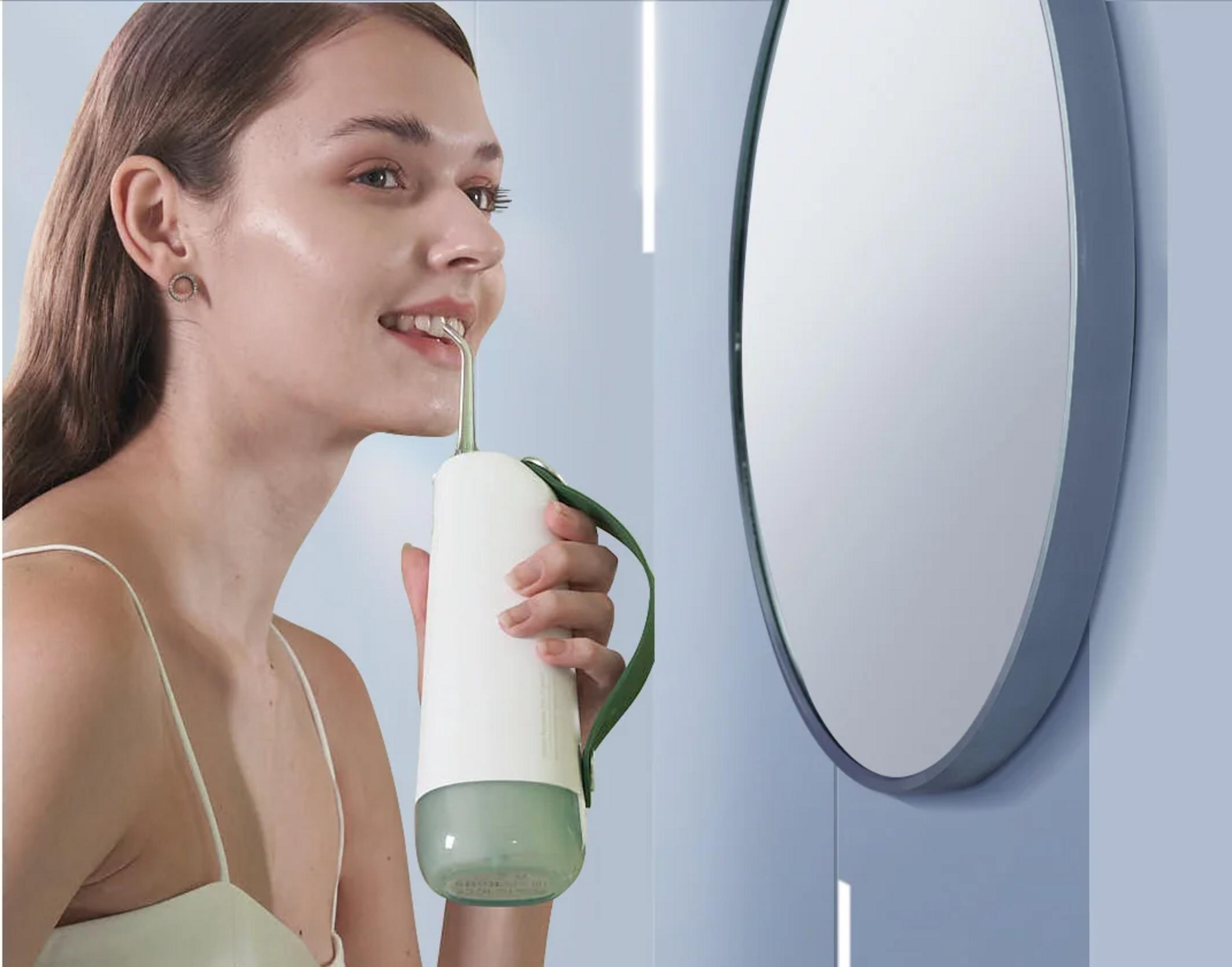 Donna usa un idropulsore dentale portatile, vicino alla bocca davanti a uno specchio.