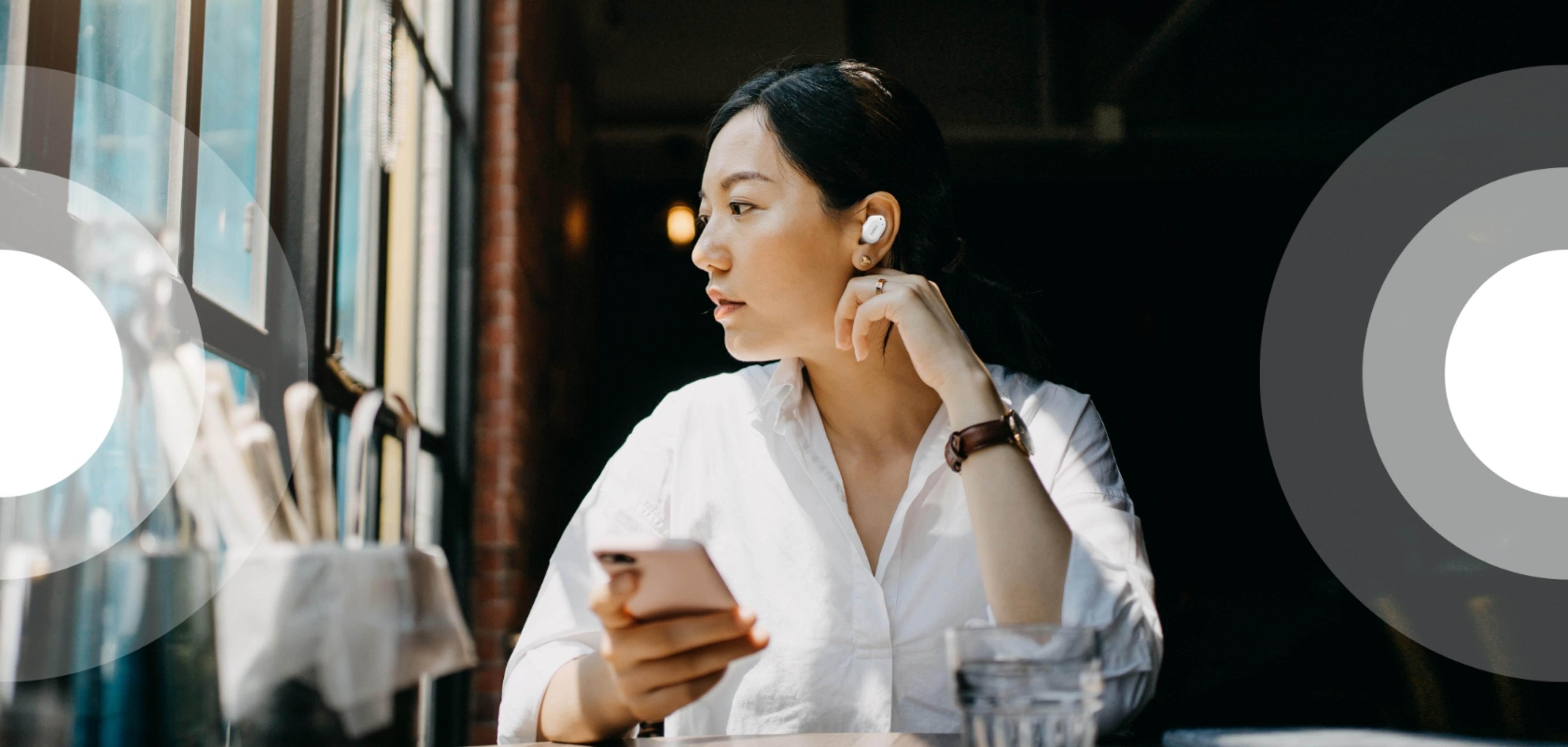 Kobieta ze słuchawkami i telefonem przy stoliku przy oknie.