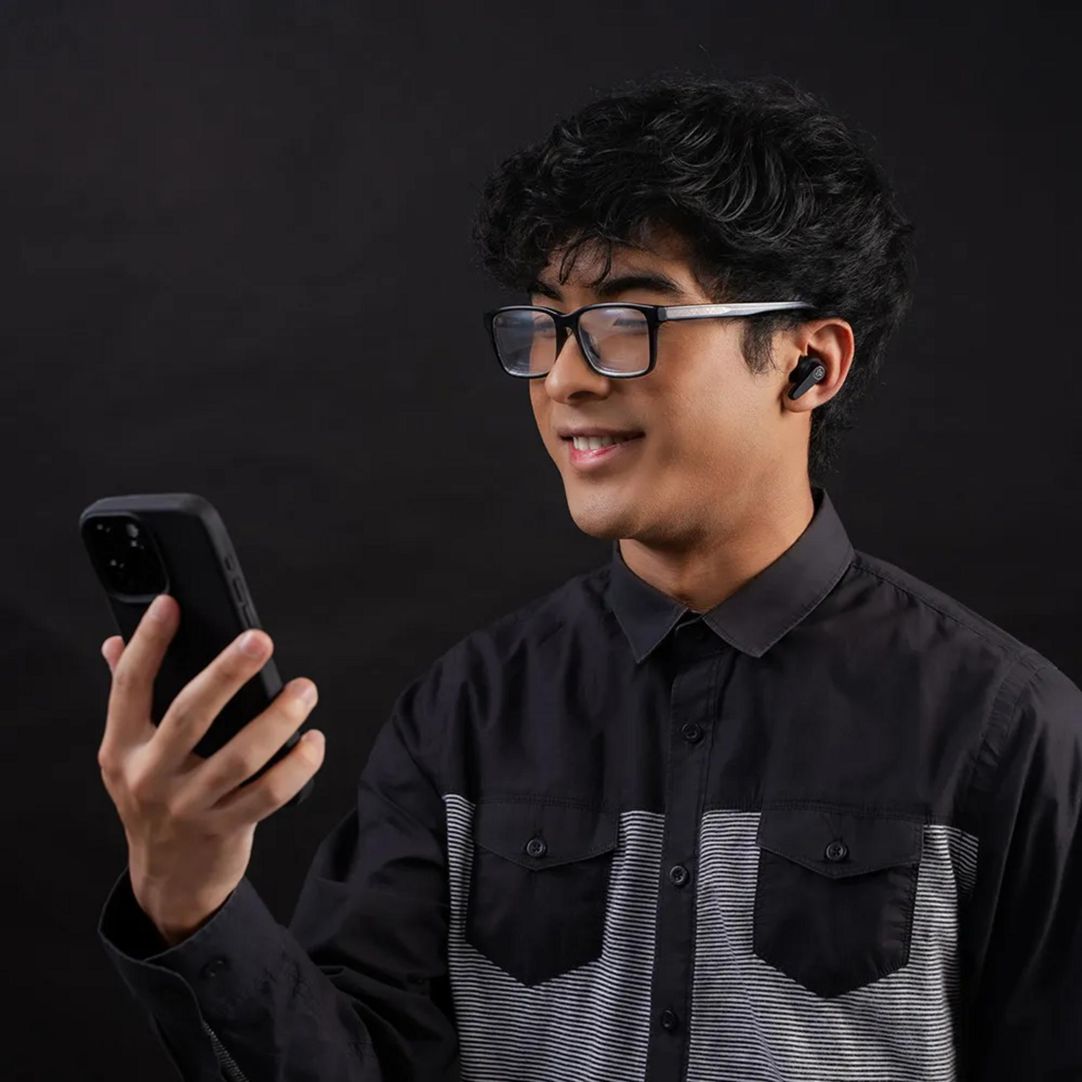 Un uomo con occhiali e auricolari tiene in mano uno smartphone.