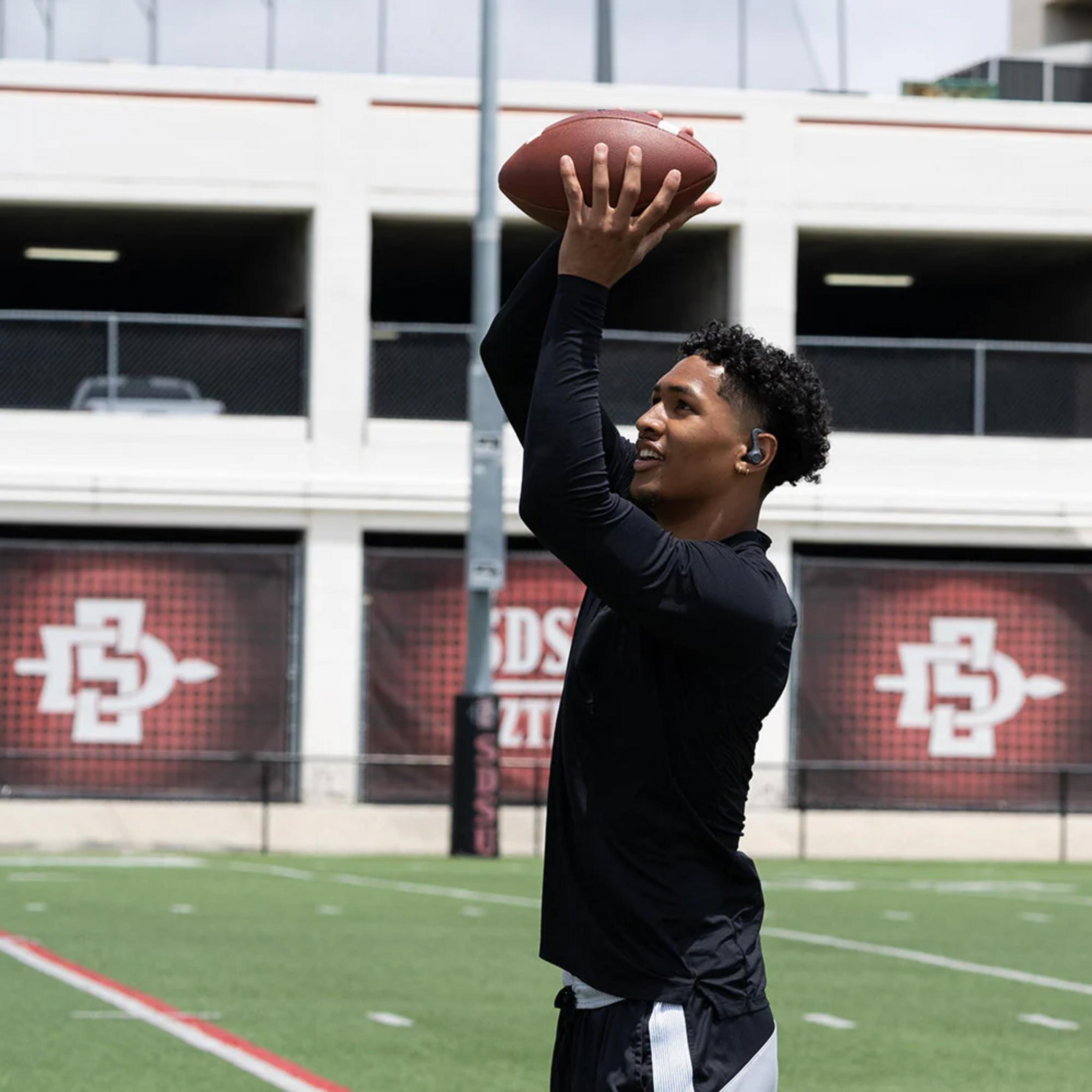 Młody mężczyzna w czerni rzuca piłkę do futbolu amerykańskiego w górę.