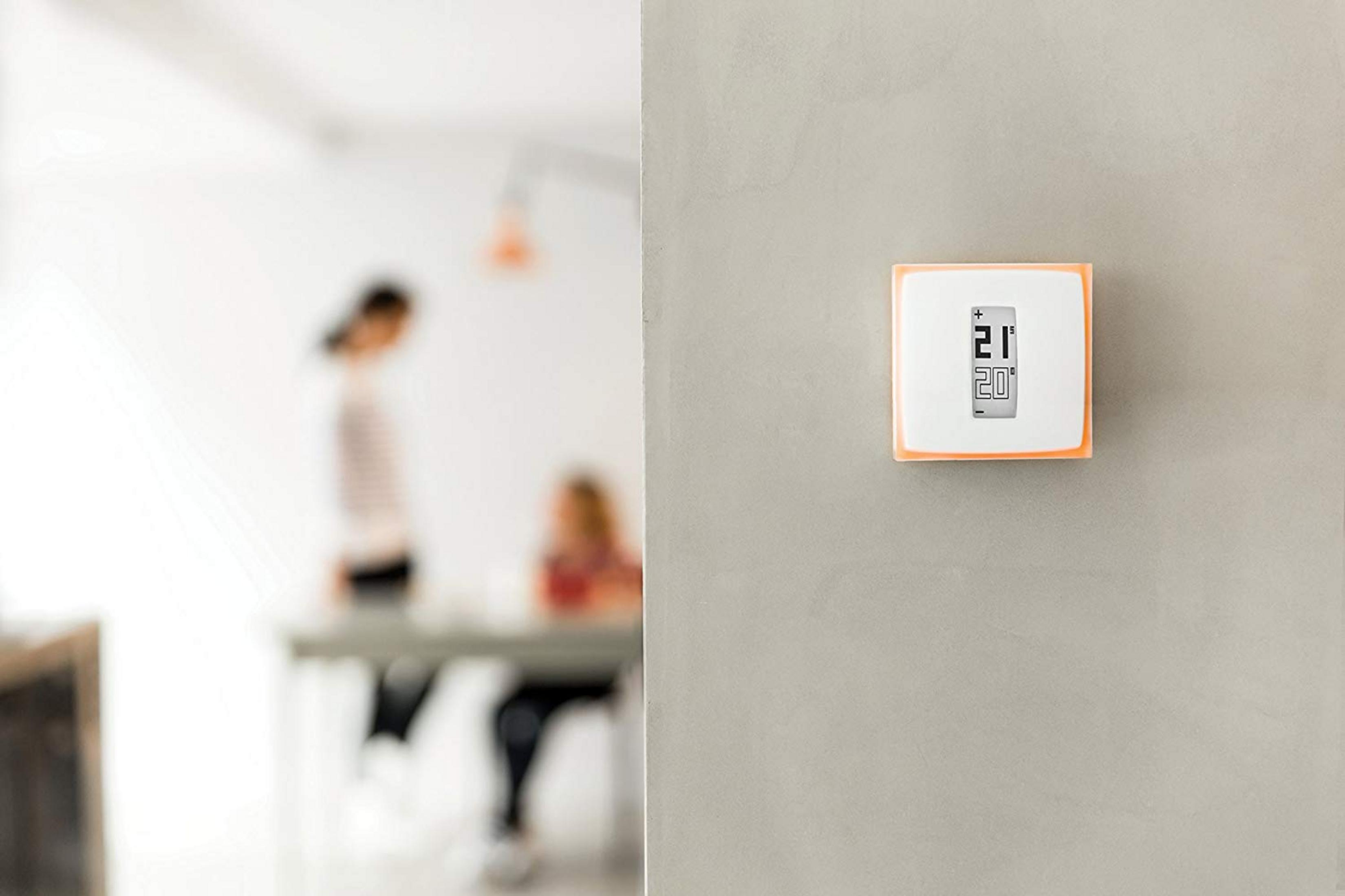 A thermostat displays 21 degrees. Blurred people are in the background.