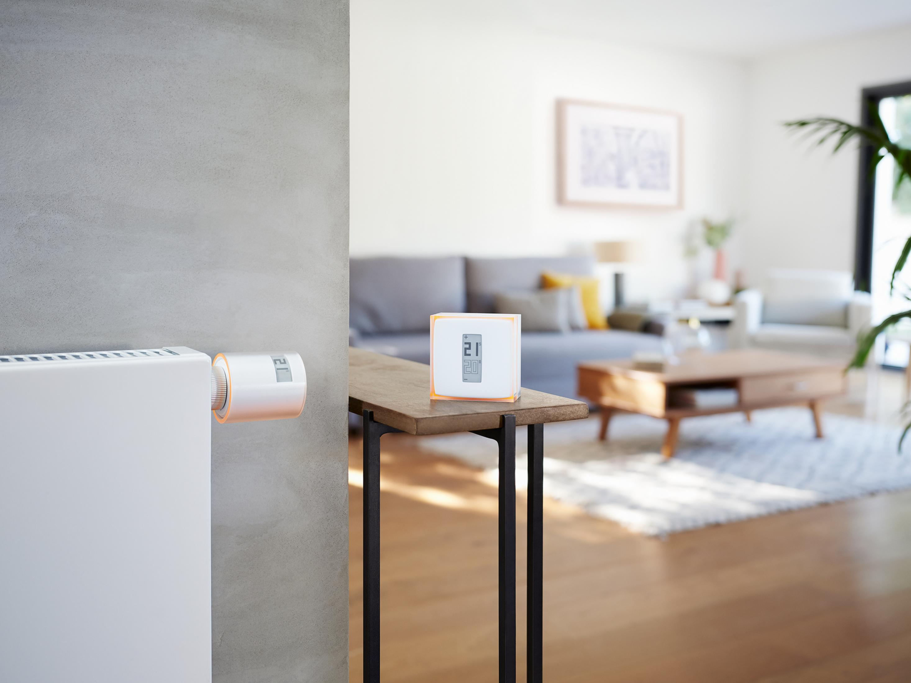 Ein Thermostat zeigt 21 Grad neben einem Heizkörper. Wohnzimmer im Hintergrund.