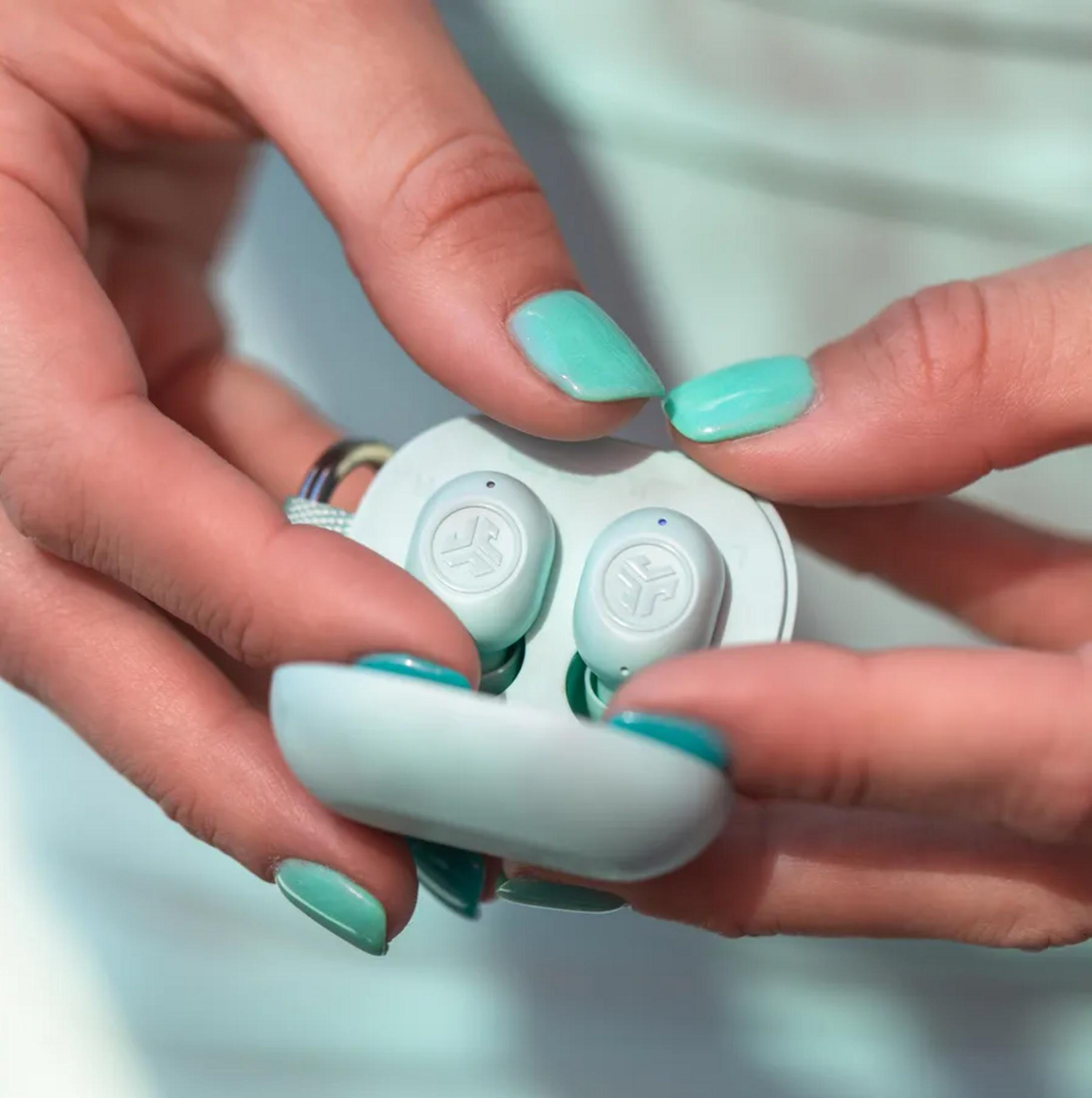 Mani con unghie verde menta tengono un astuccio verde menta e bianco con auricolari.