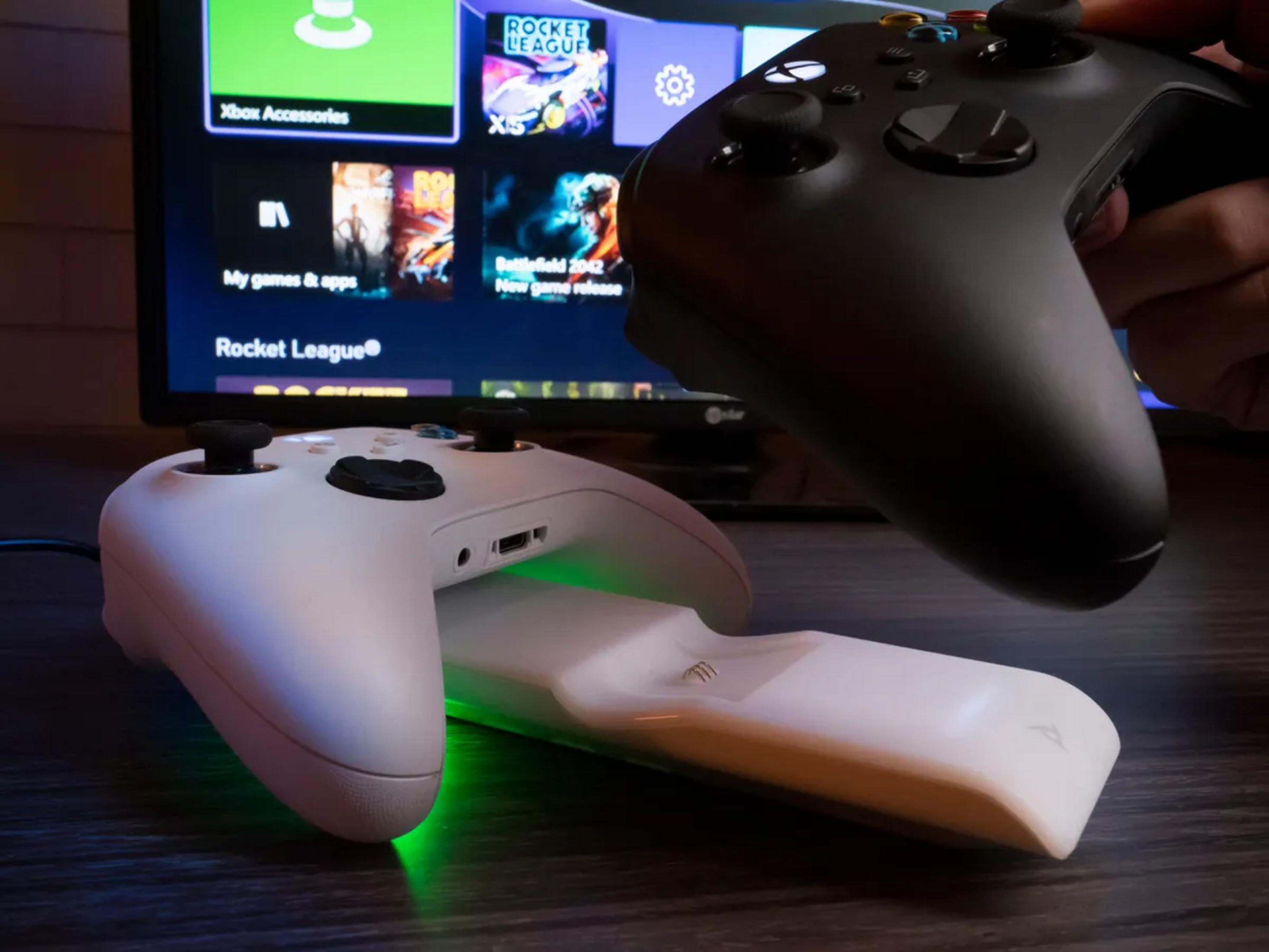 Dwa kontrolery Xbox, jeden biały, jeden czarny, przed ekranem z grami.