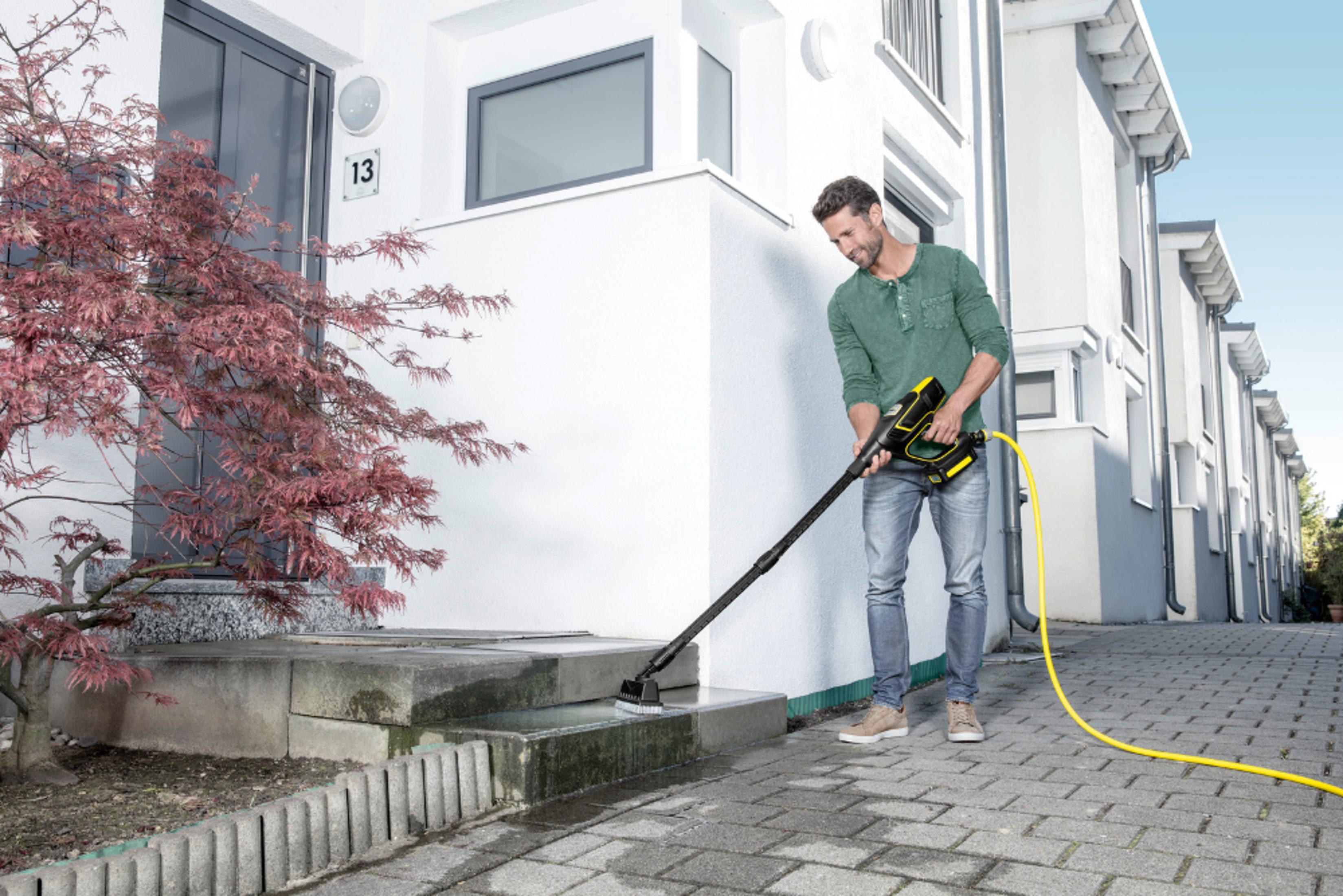 Mężczyzna czyści stopnie myjką ciśnieniową przed nowoczesnym domem