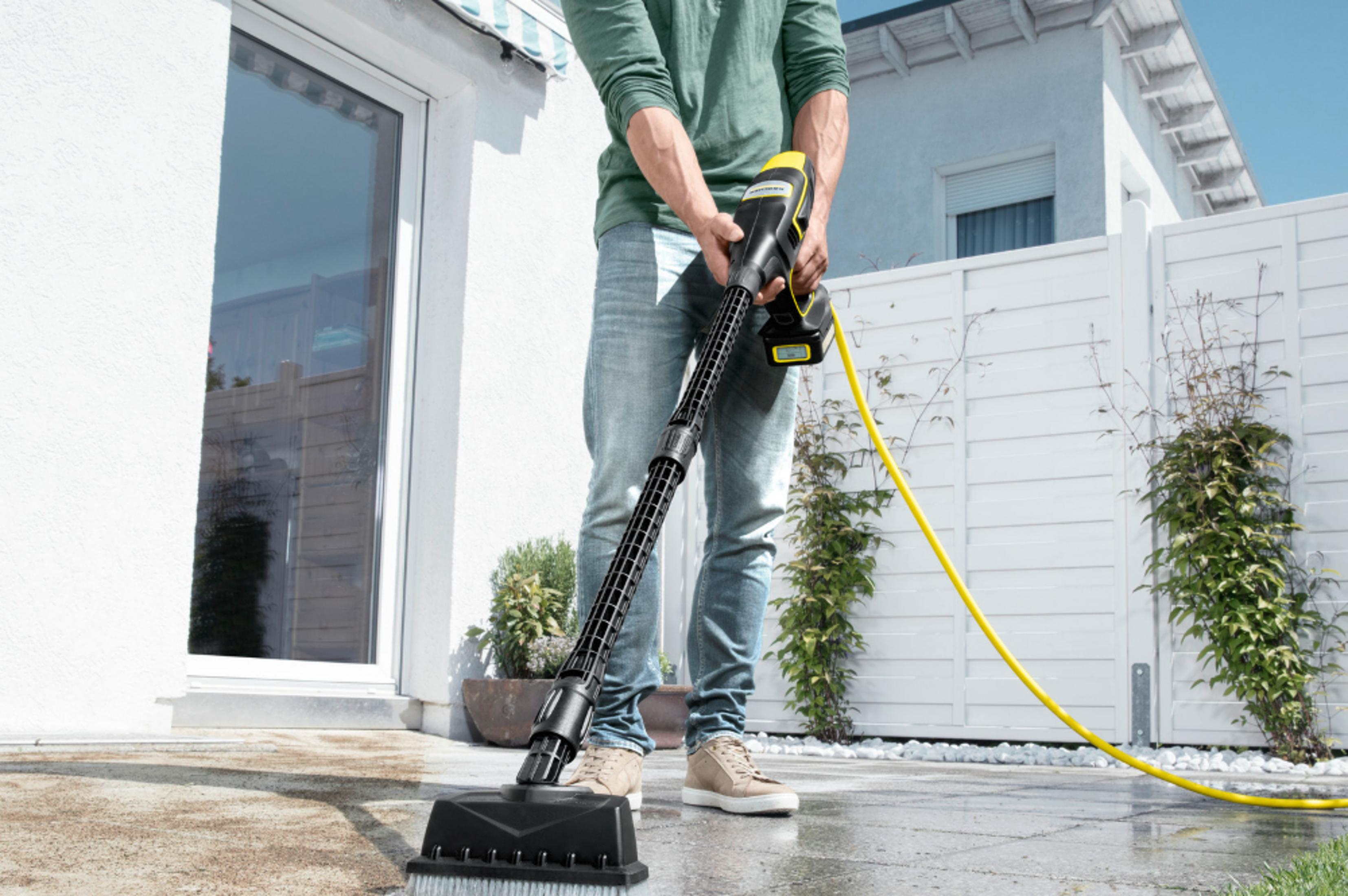 Mężczyzna czyści taras myjką ciśnieniową. Widoczny żółty wąż.