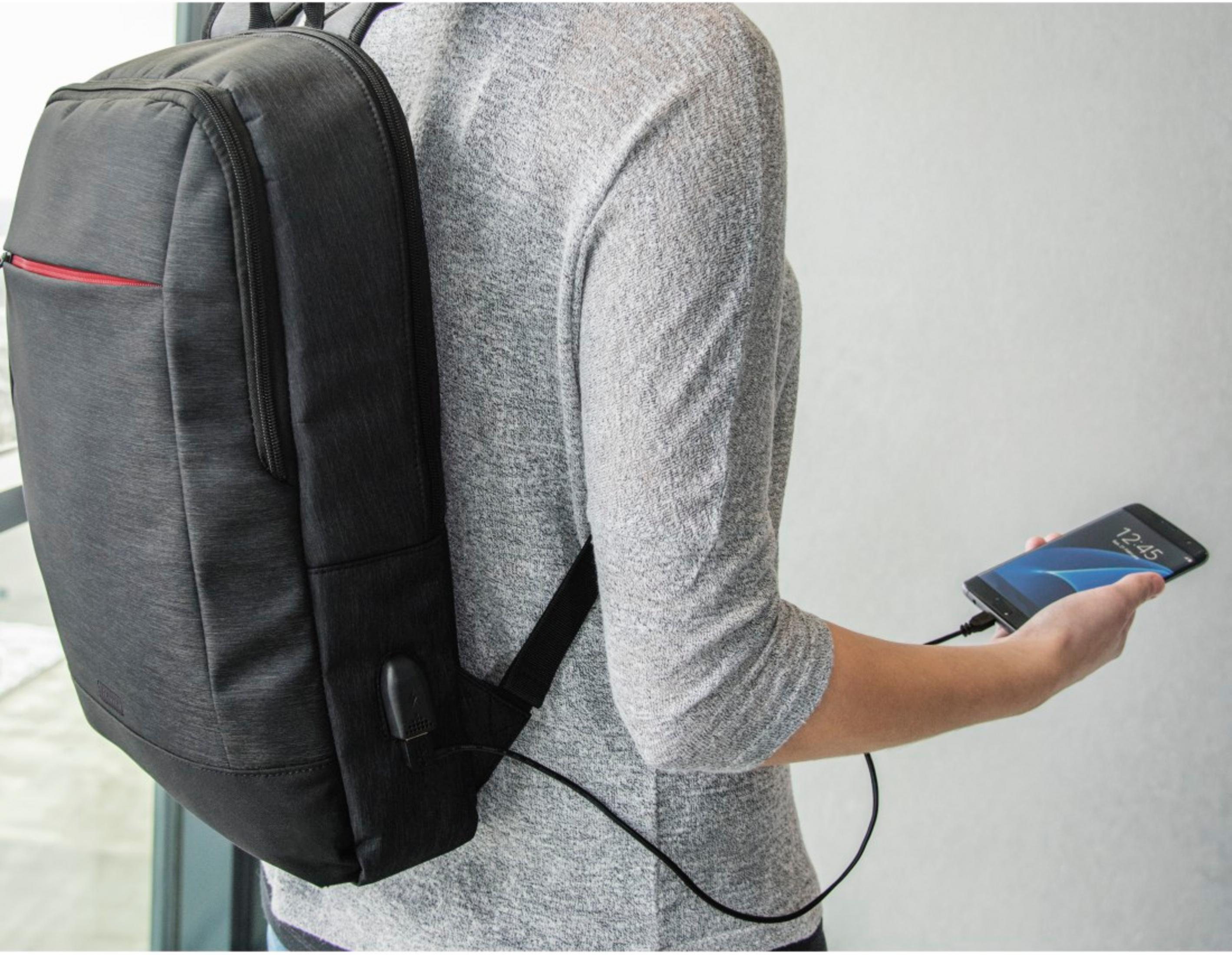 Una persona con maglione grigio carica uno smartphone tramite uno zaino.