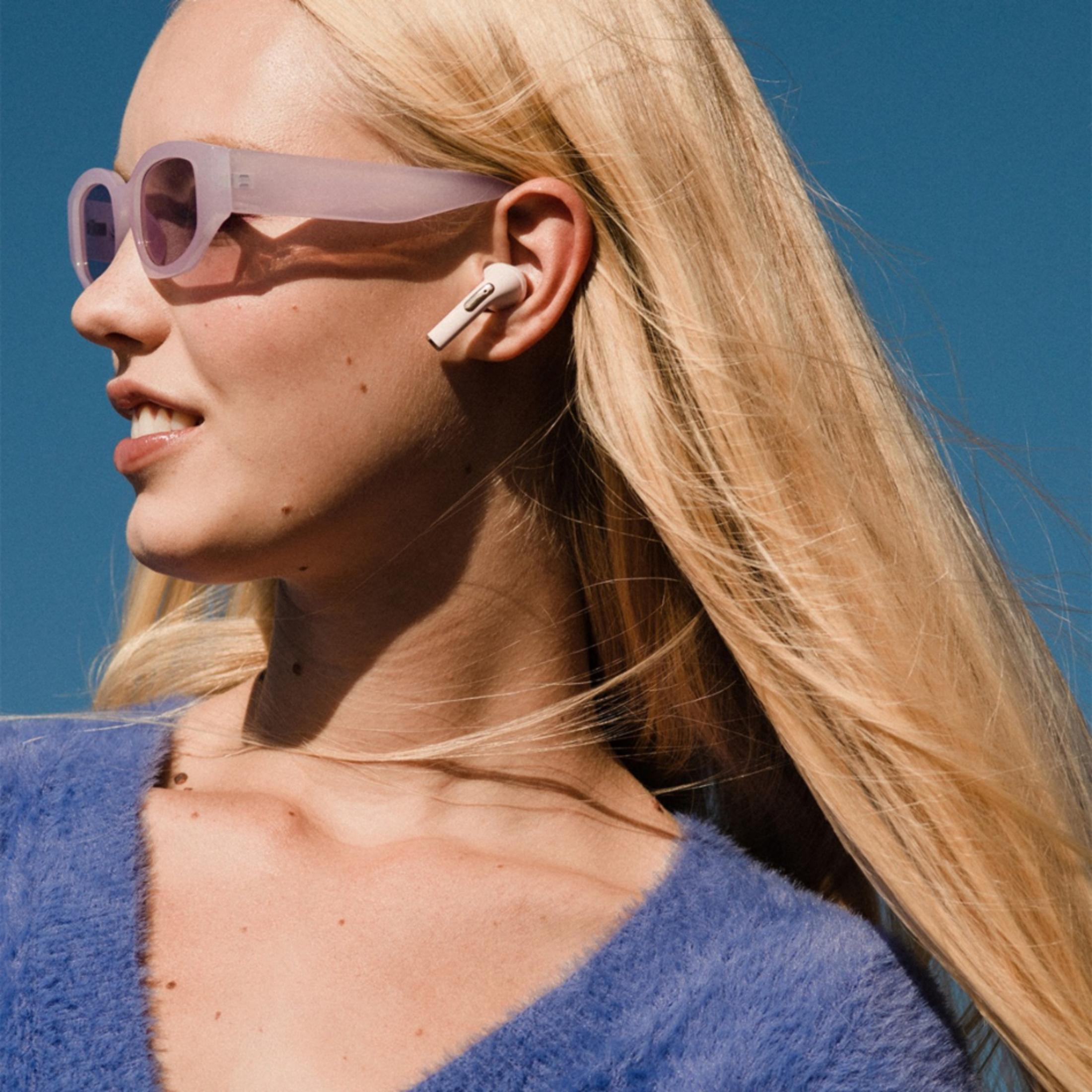 Eine Frau mit blonden Haaren trägt Kopfhörer und eine Sonnenbrille.
