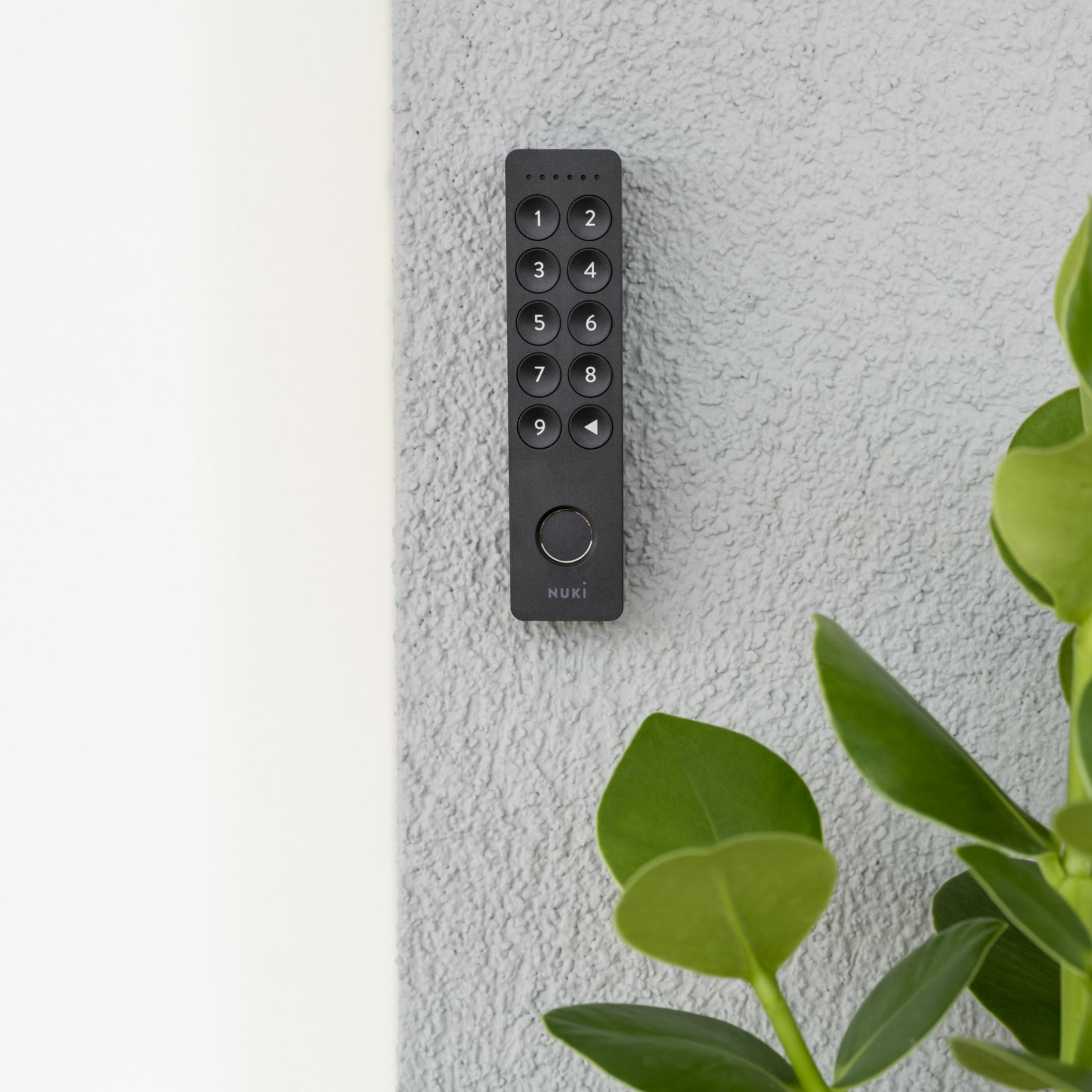 Een zwart Nuki Keypad met de cijfers 1-9 op een grijze, gestructureerde muur.