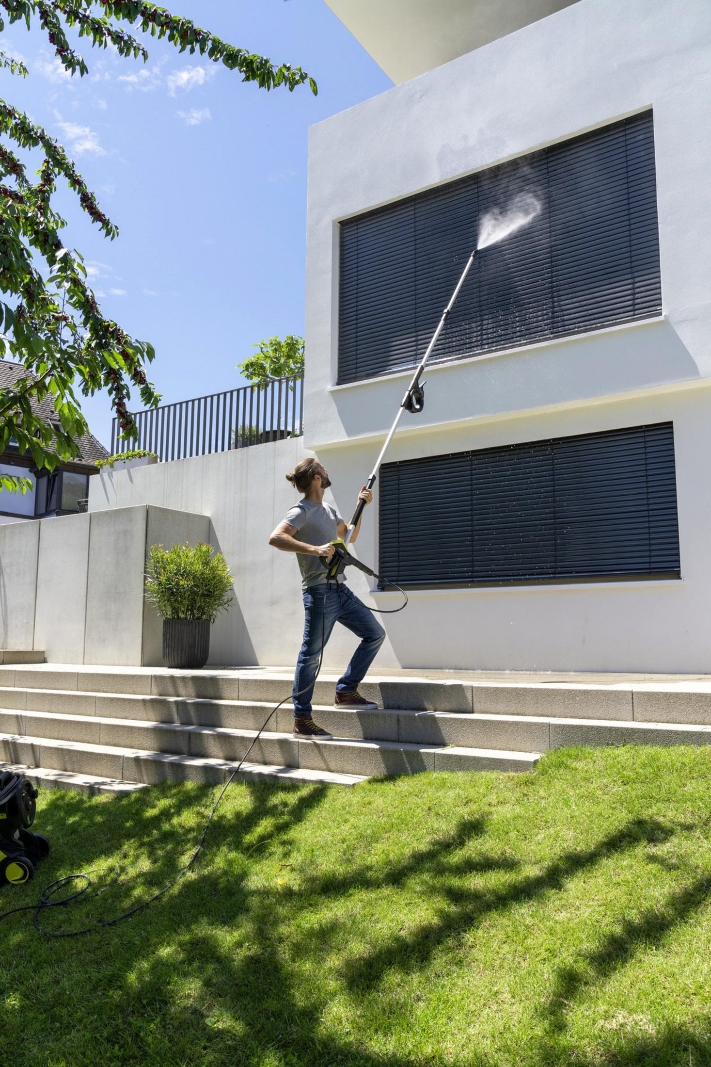 Hombre limpia ventana con hidrolimpiadora en escalones junto a casa moderna.