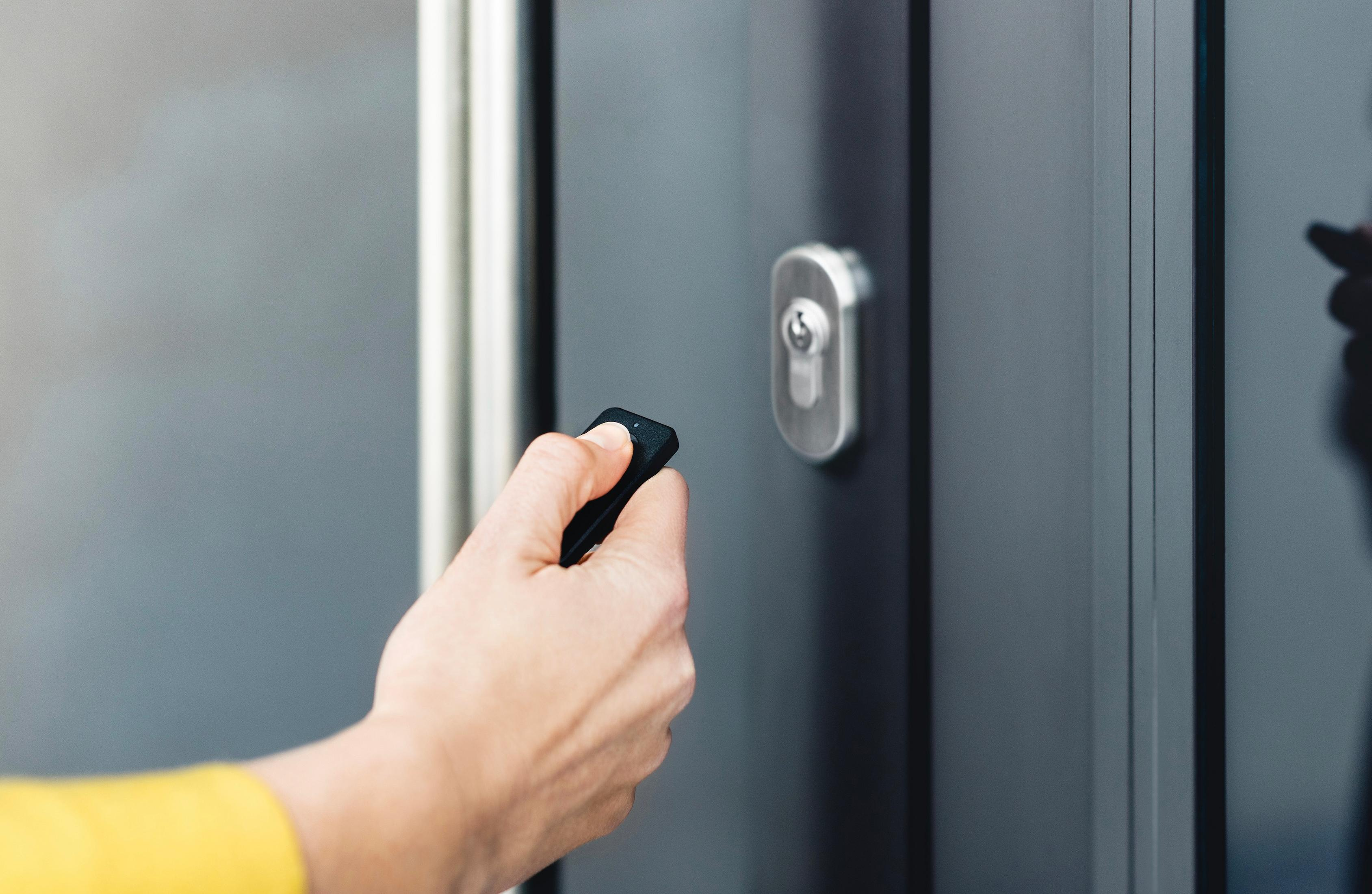 A hand holds a black remote near a dark door with a keyhole.