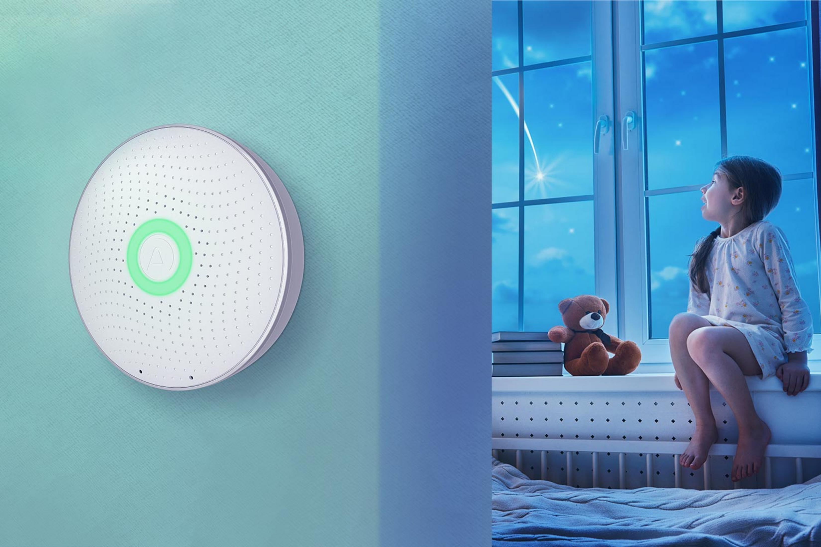 Runder weißer Sensor mit grünem Ring hängt an Wand, daneben ein Kind.