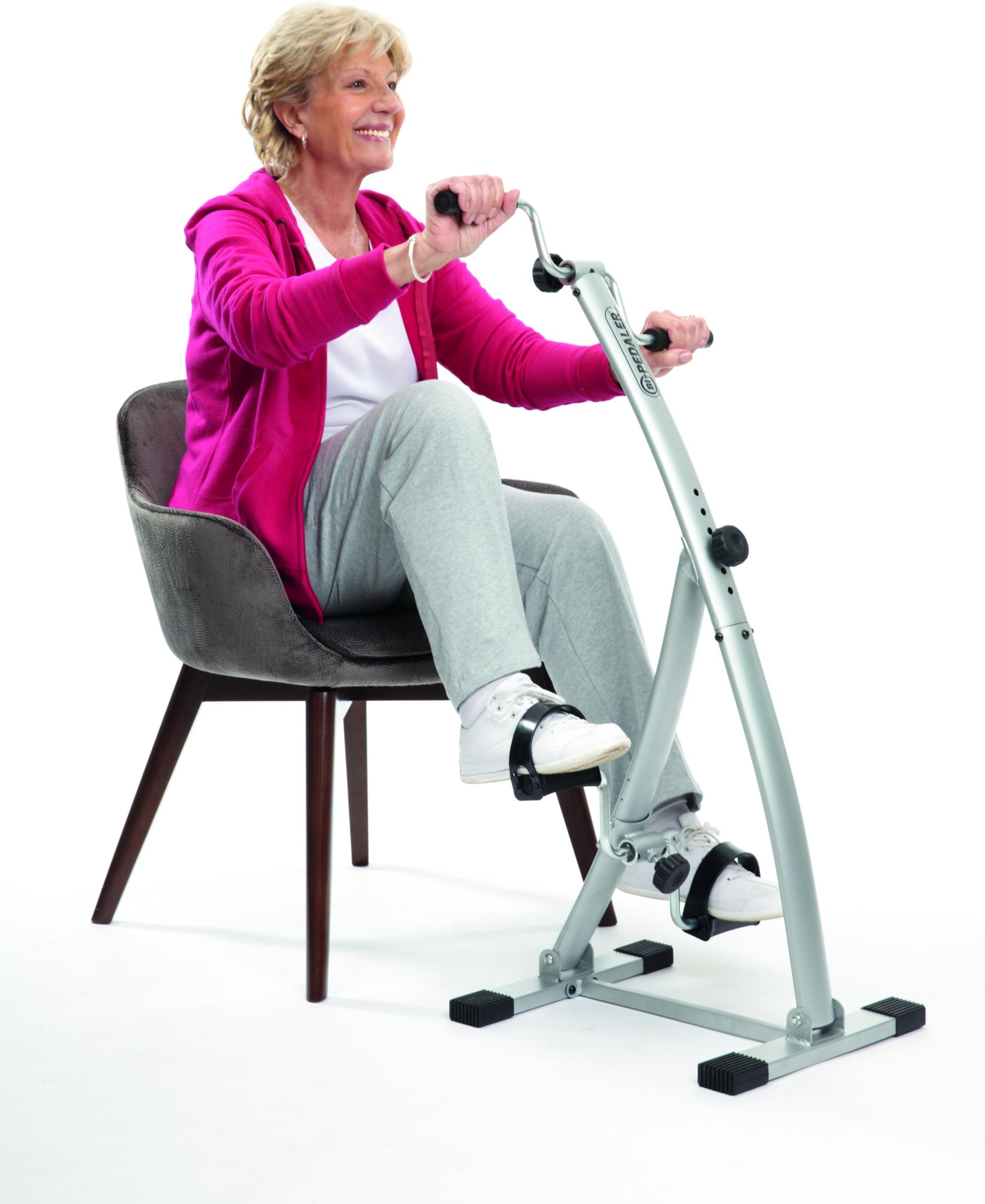 Eine Frau in Trainingskleidung sitzt auf einem Stuhl und benutzt ein silbernes Heimtrainer-Pedalgerät.