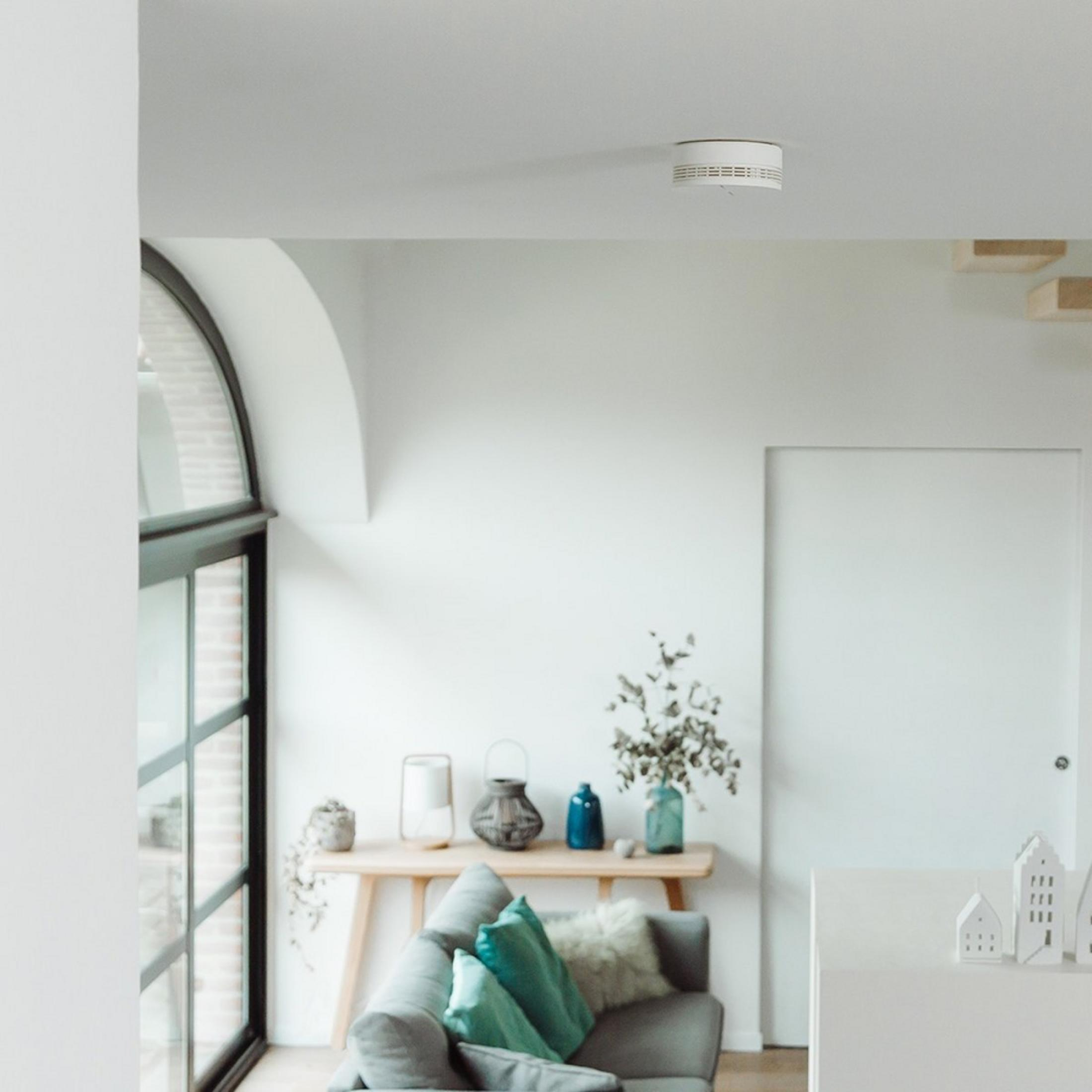 A smoke detector on the ceiling above a sofa with cushions.